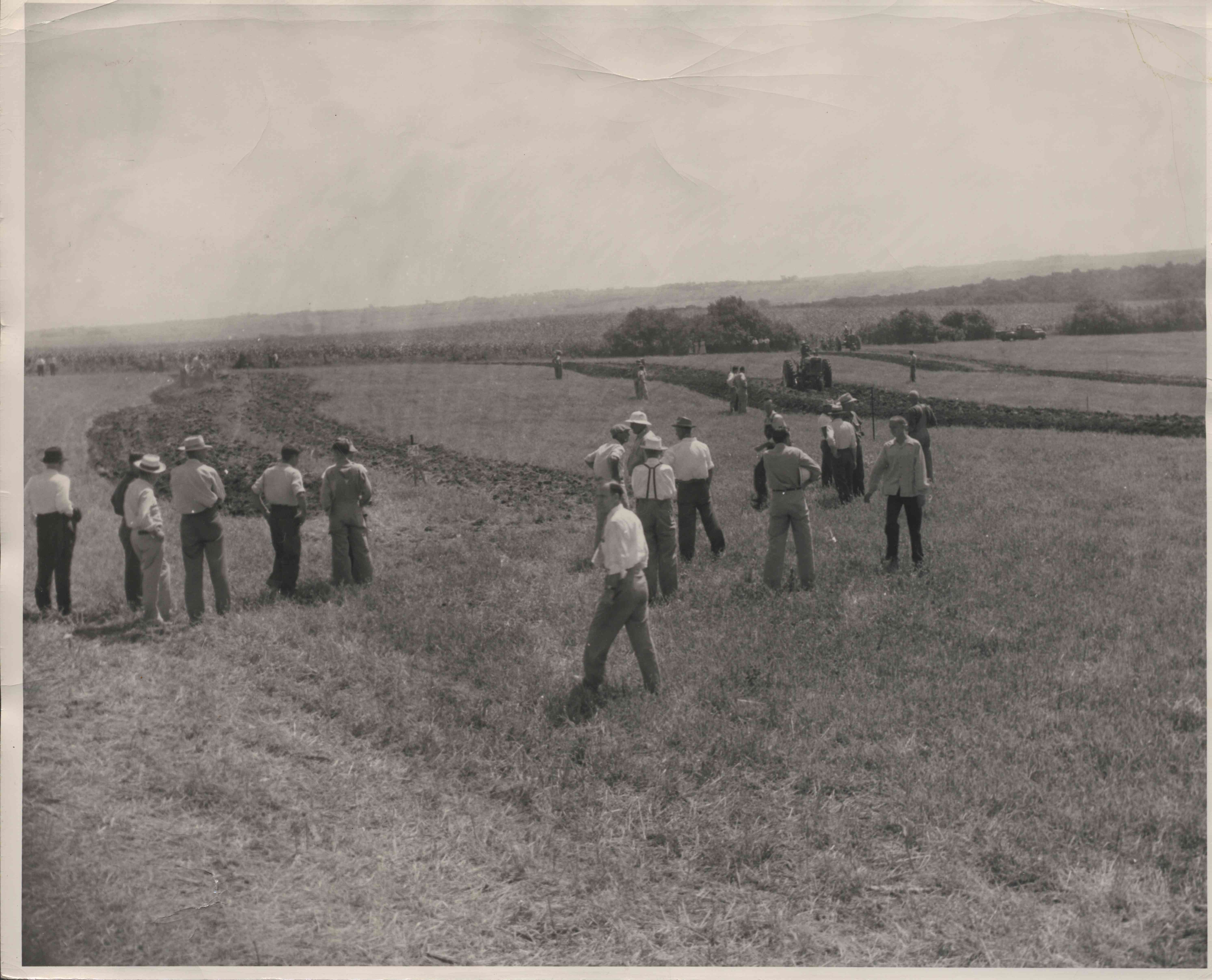 Group of men in field watching tractors plow field