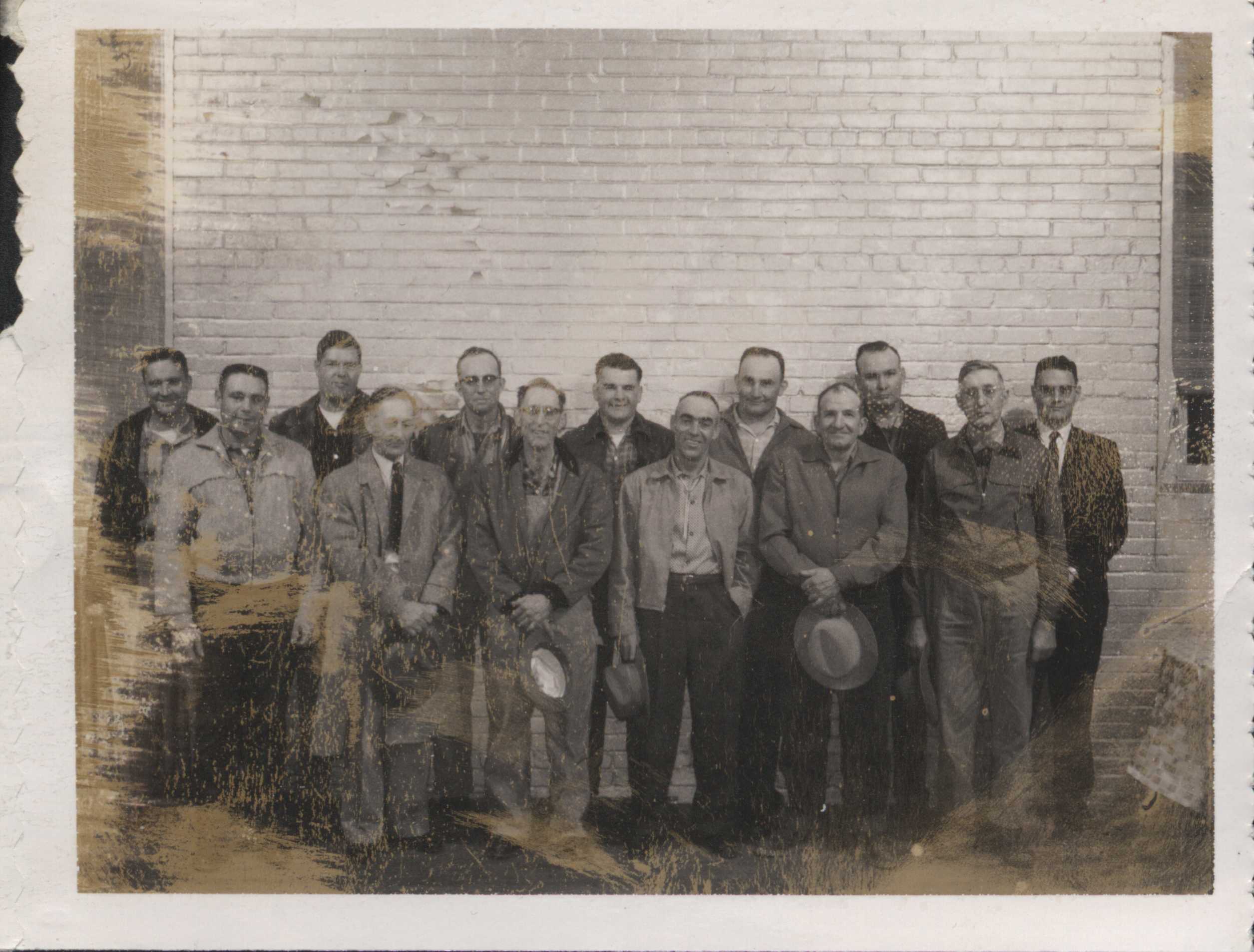 Gathering of unidentified men posing in front of white brick wall