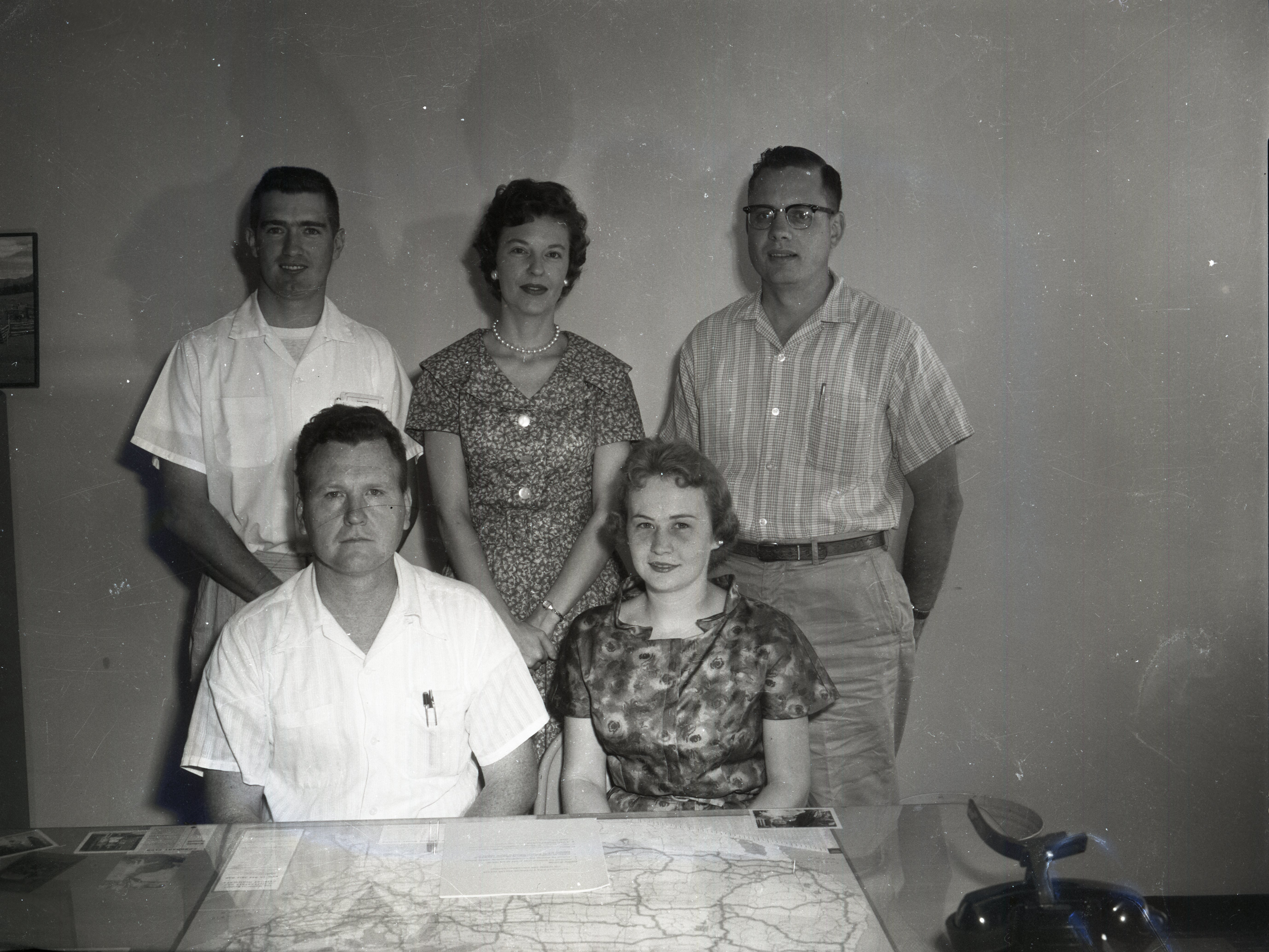 Three men and two women pose for picture in front of map