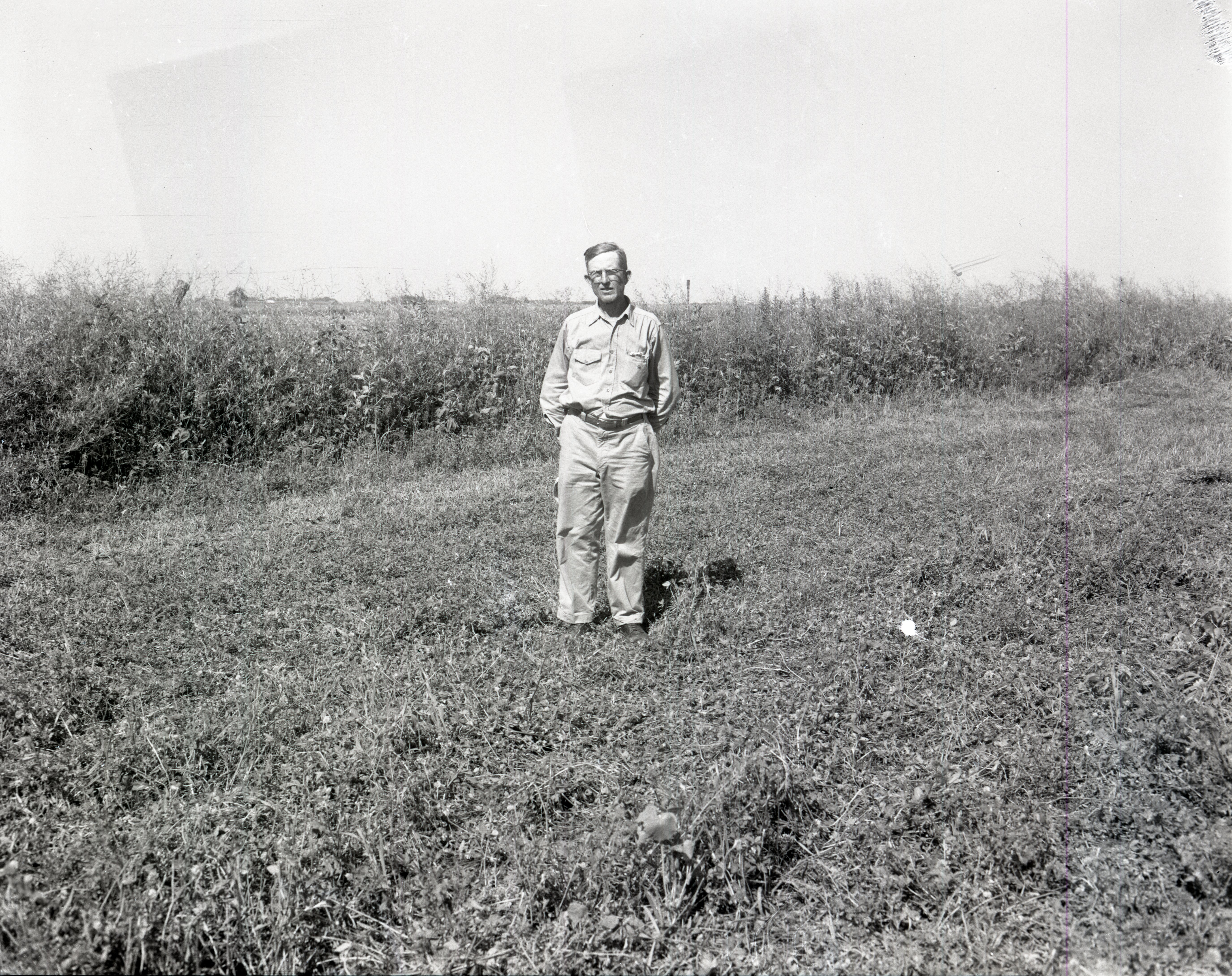 Unidentified man wearing glasses with hands behind his back stands in field