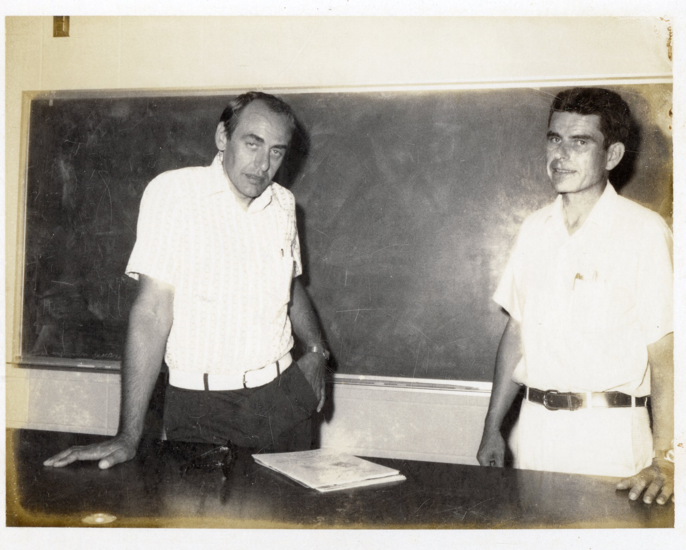 1970s Two unidentified men stand in front of chalkboard