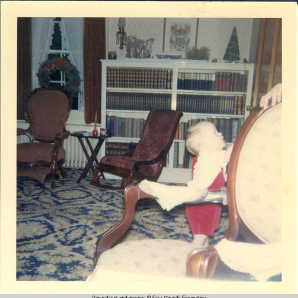 John, Jr. standing in the parlor by chair
