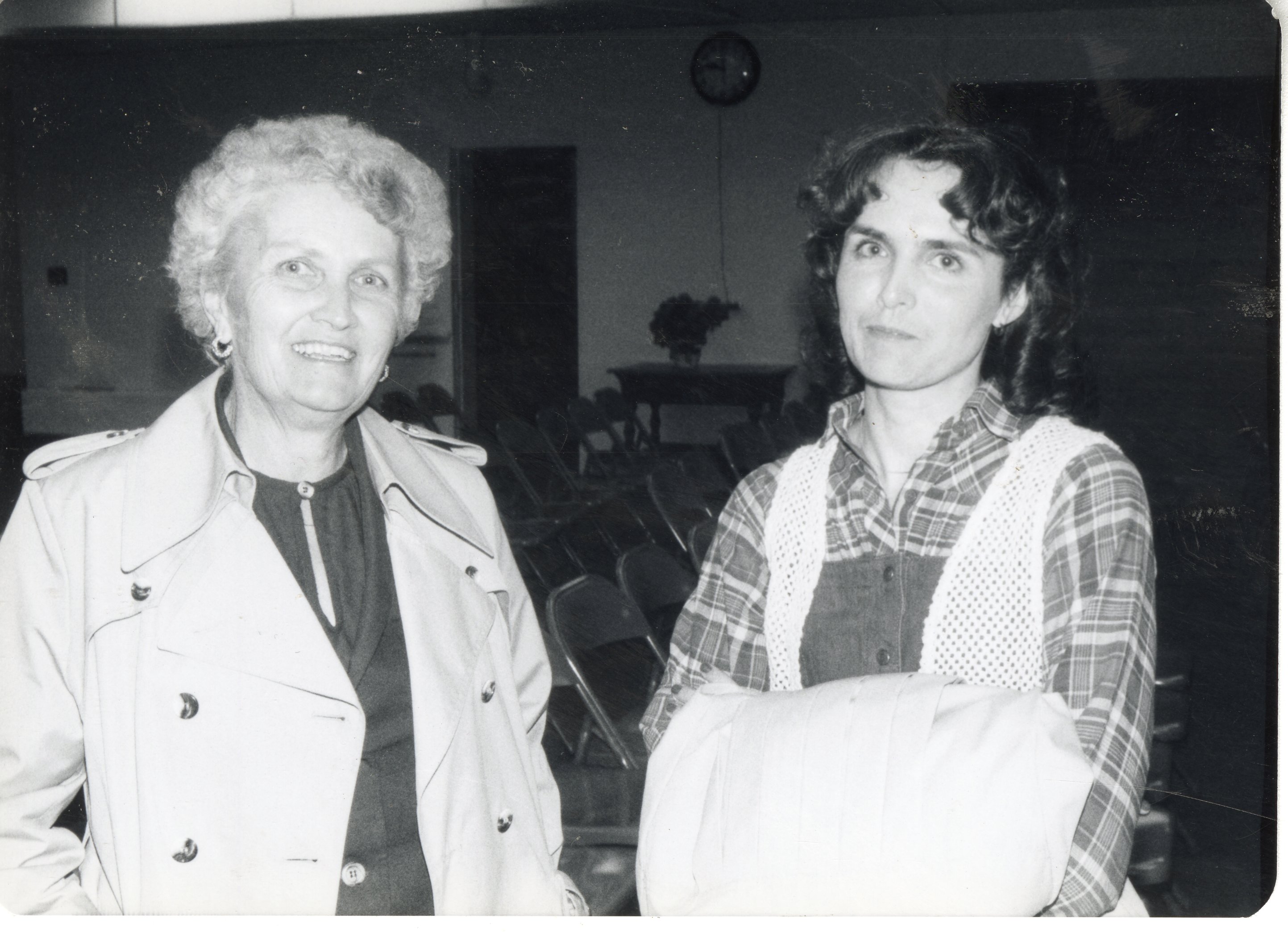 Two unidentified women pose for photo in a room with folding chairs