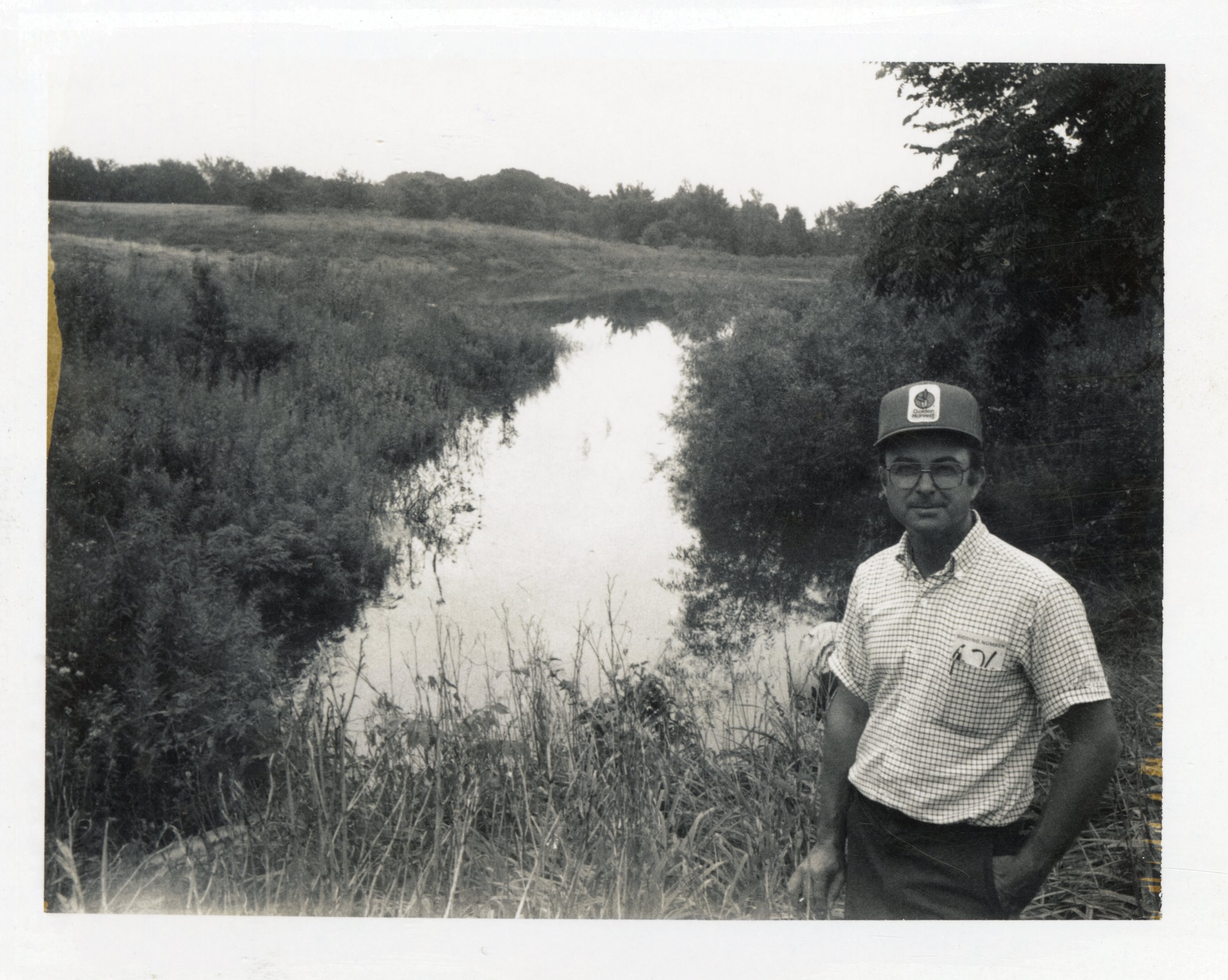 1986 Bill Walker stands by water  in field