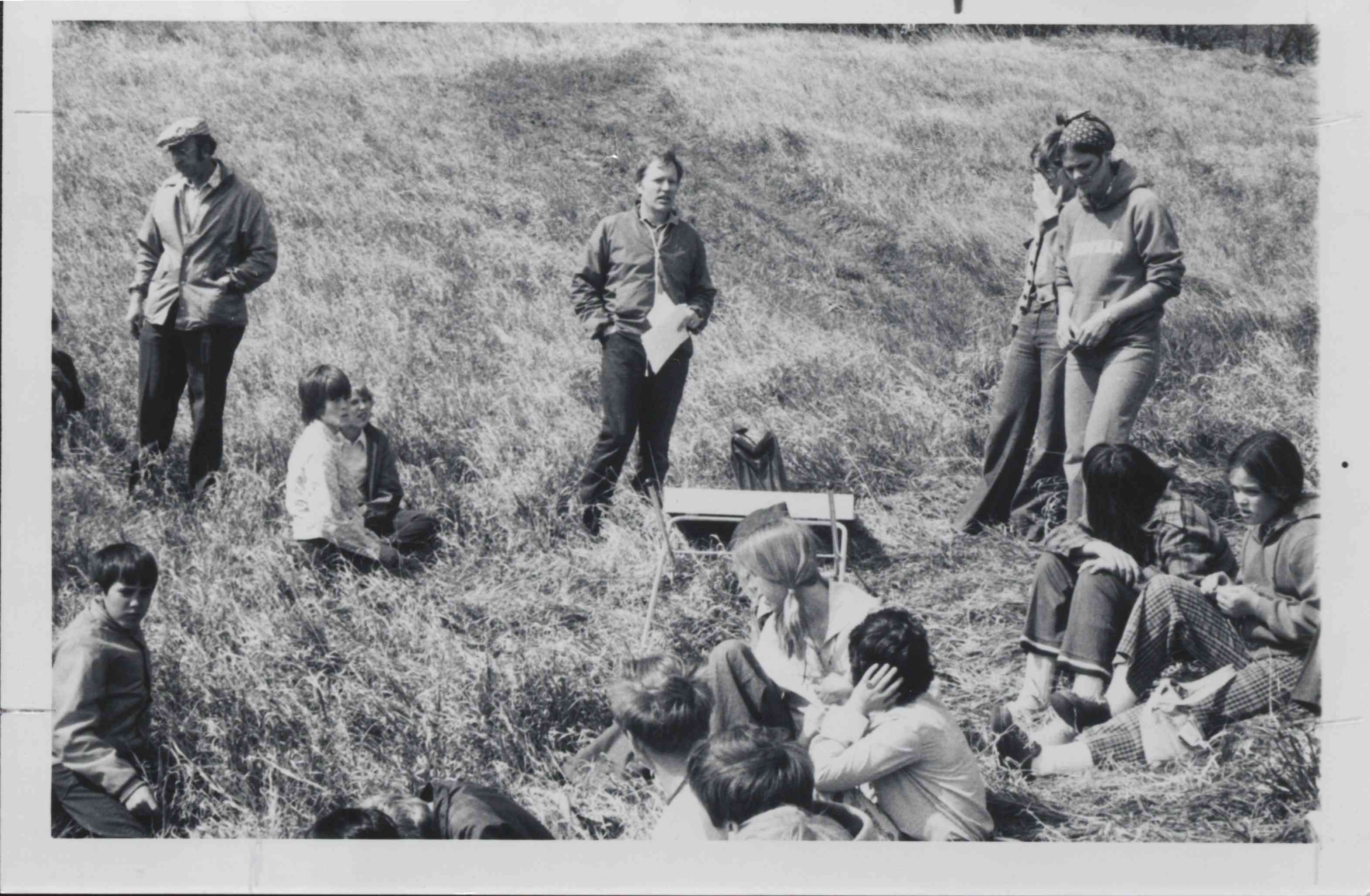 Man Holding Papers Gives Talk to Students sitting in grass
