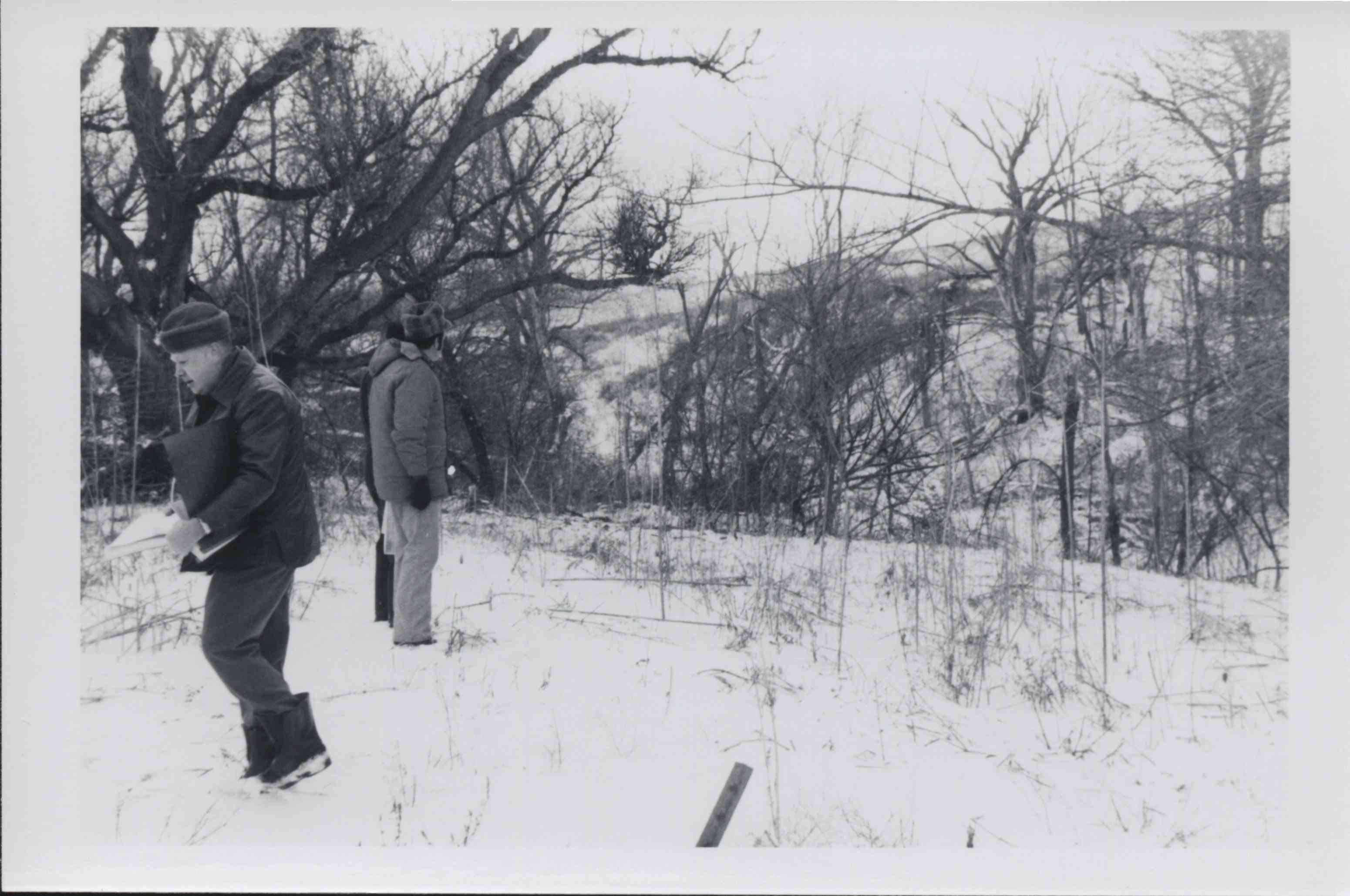 Two unidentified men stand in the snow looking toward an enbankment while another man walks in the opposite direction