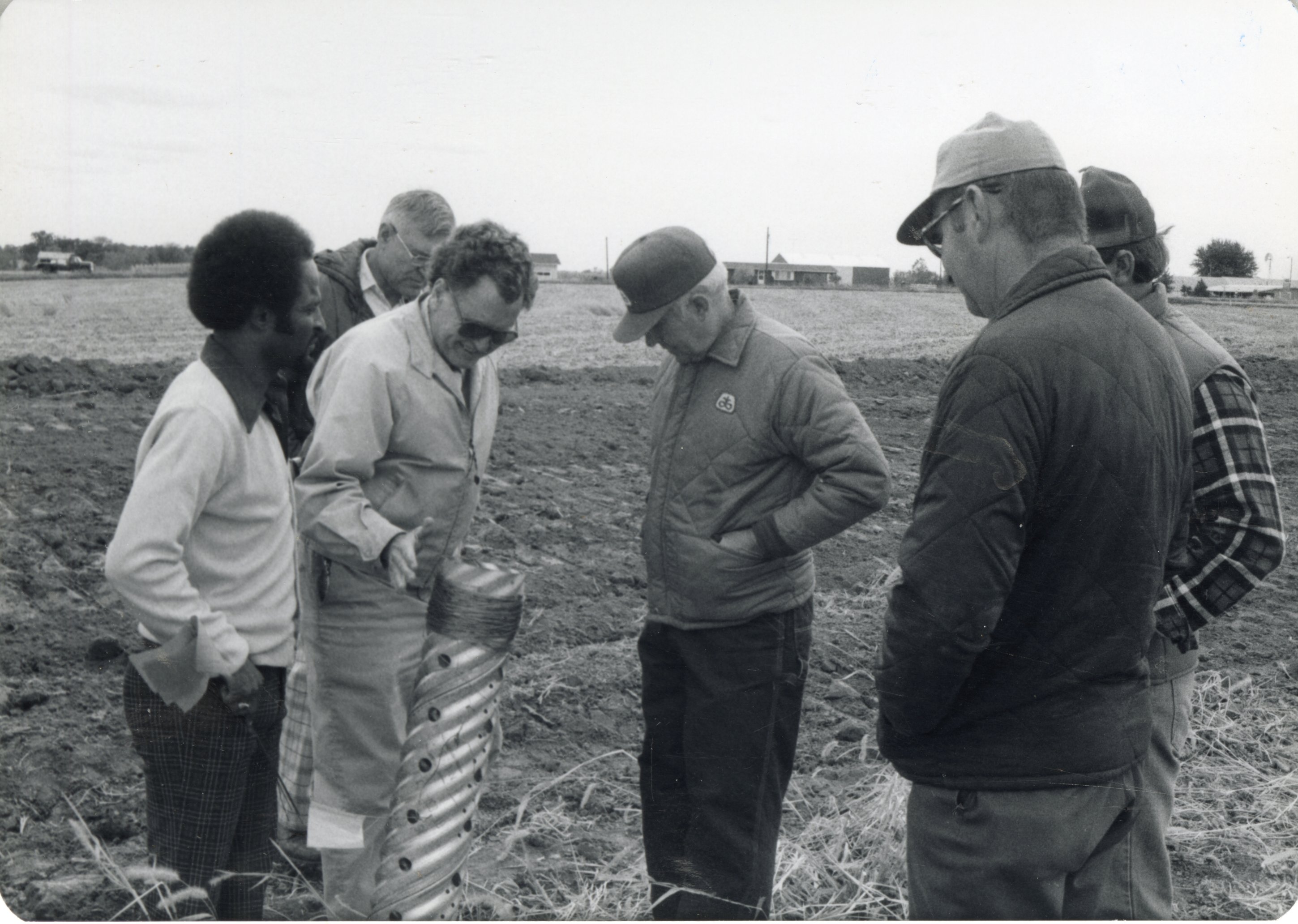 Six men examine drainage pipe in field