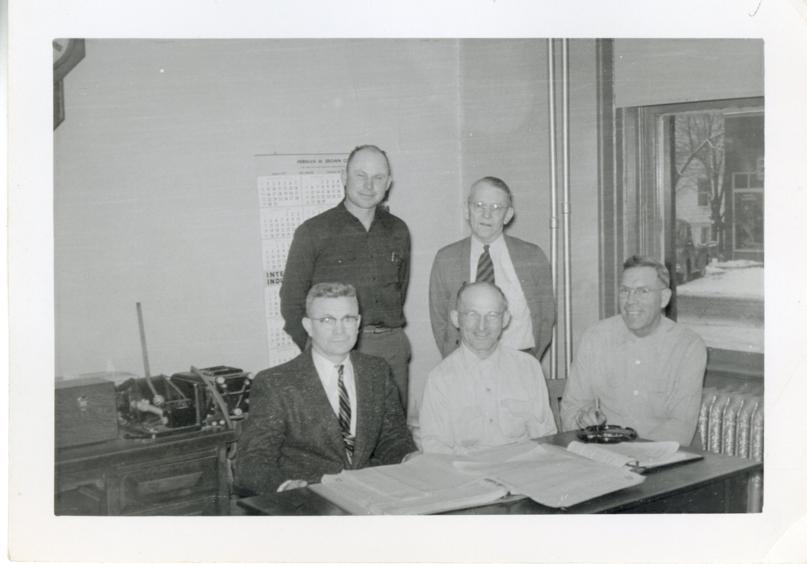 Two Men Standing and Three Men sitting in Office