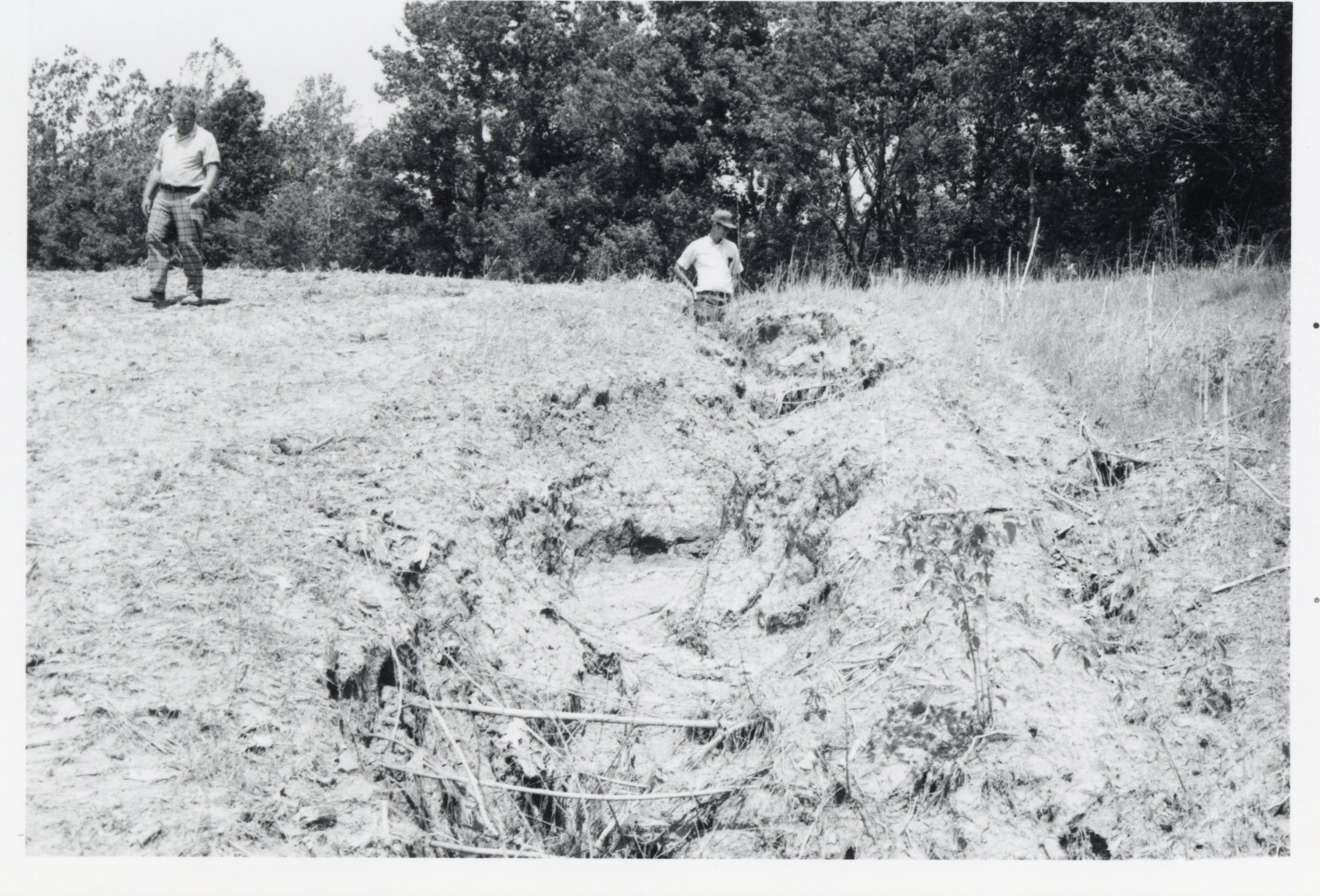 Two men look at eroded area in field