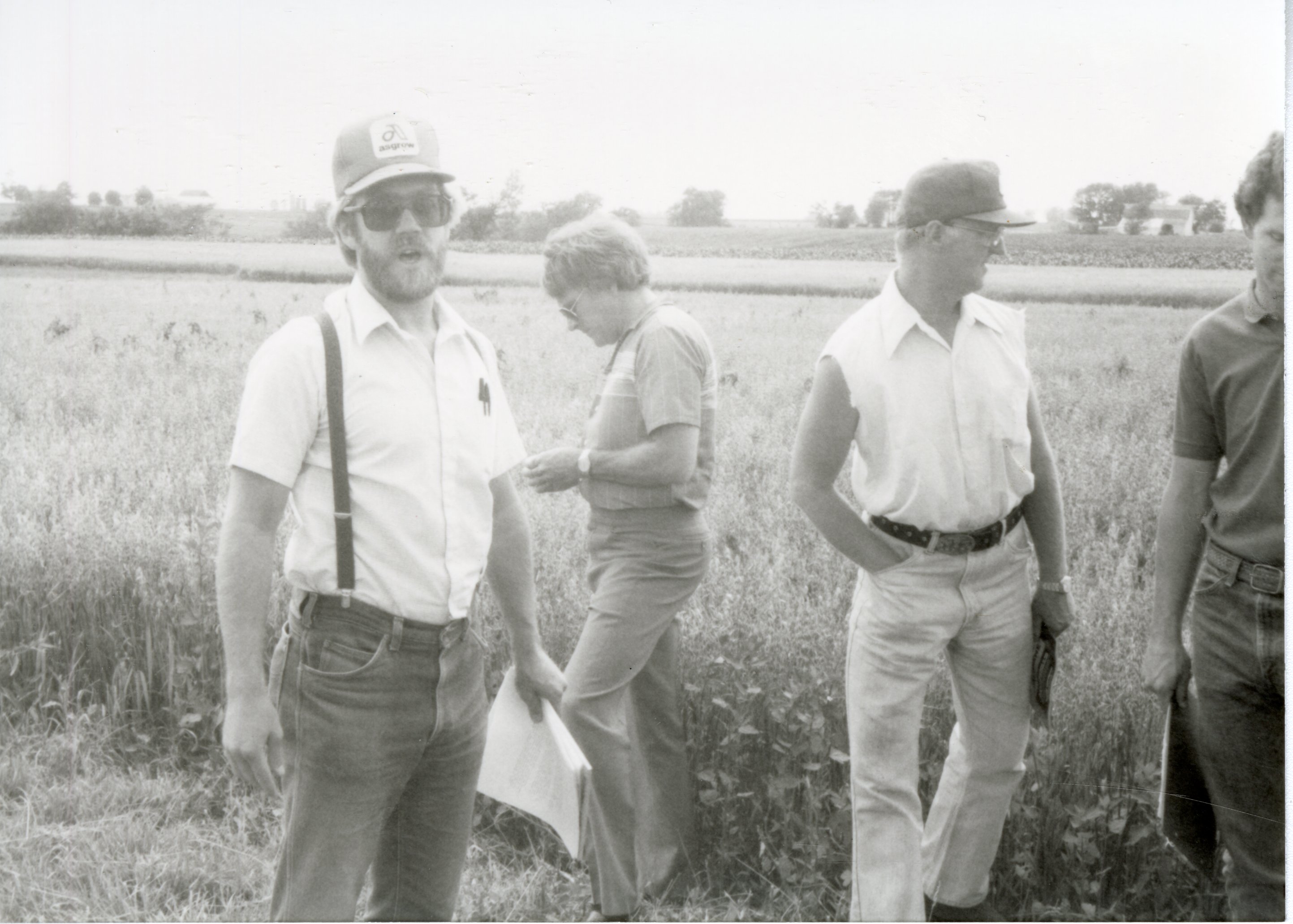 Four unidentified men stand in field by highway