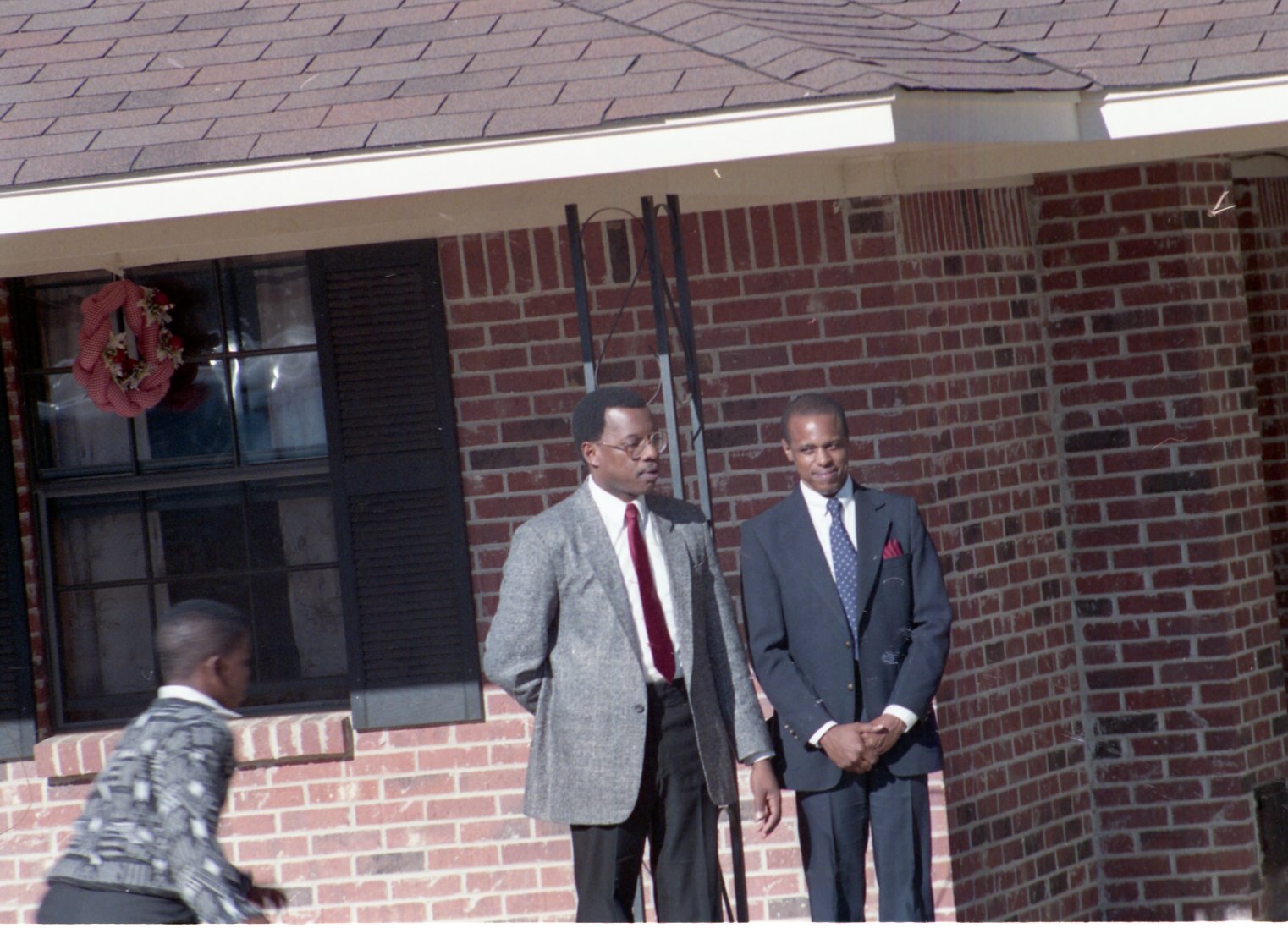 Two unidentified men and a boy stand by a brick building