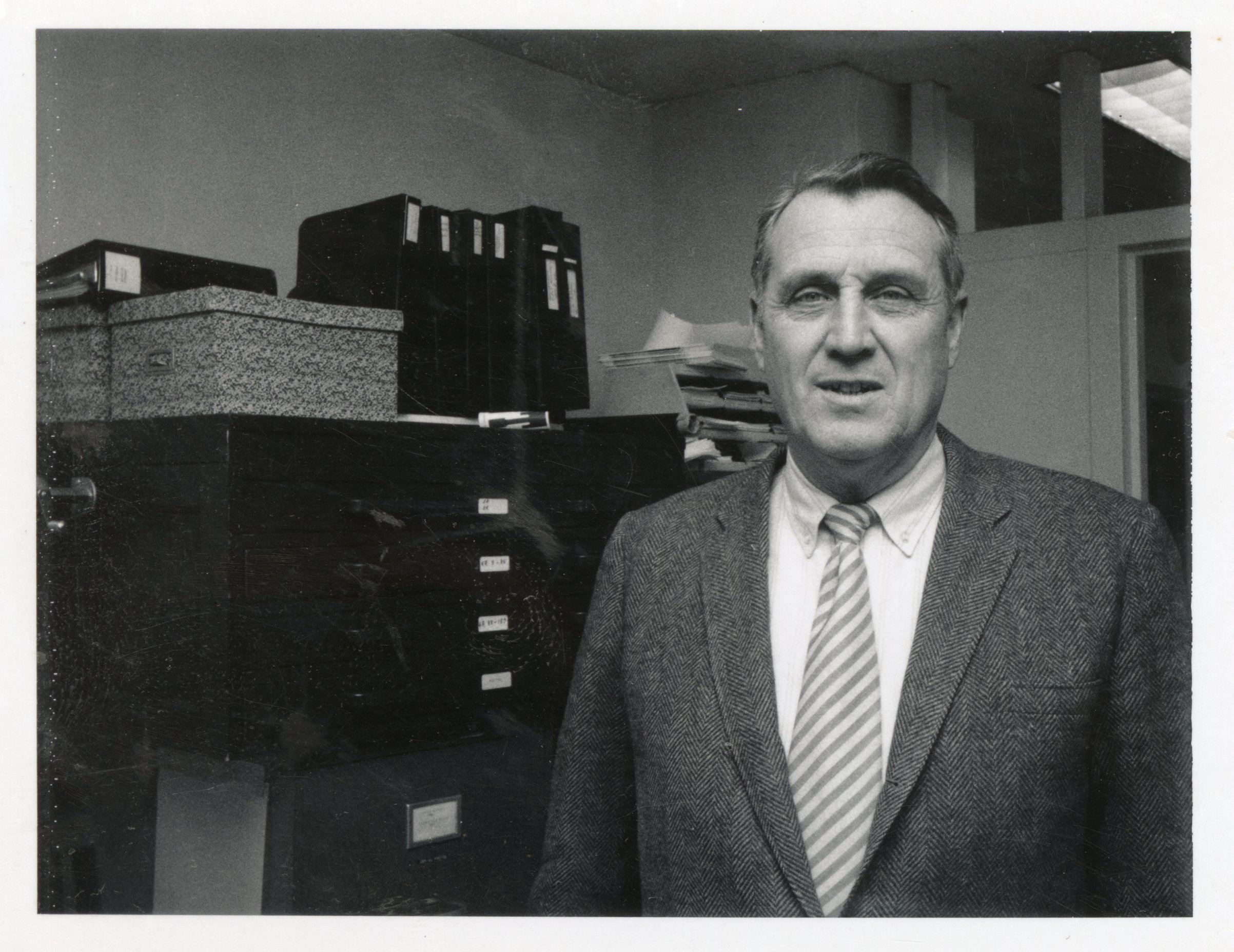 1970s Unidentified man in suit stands in office
