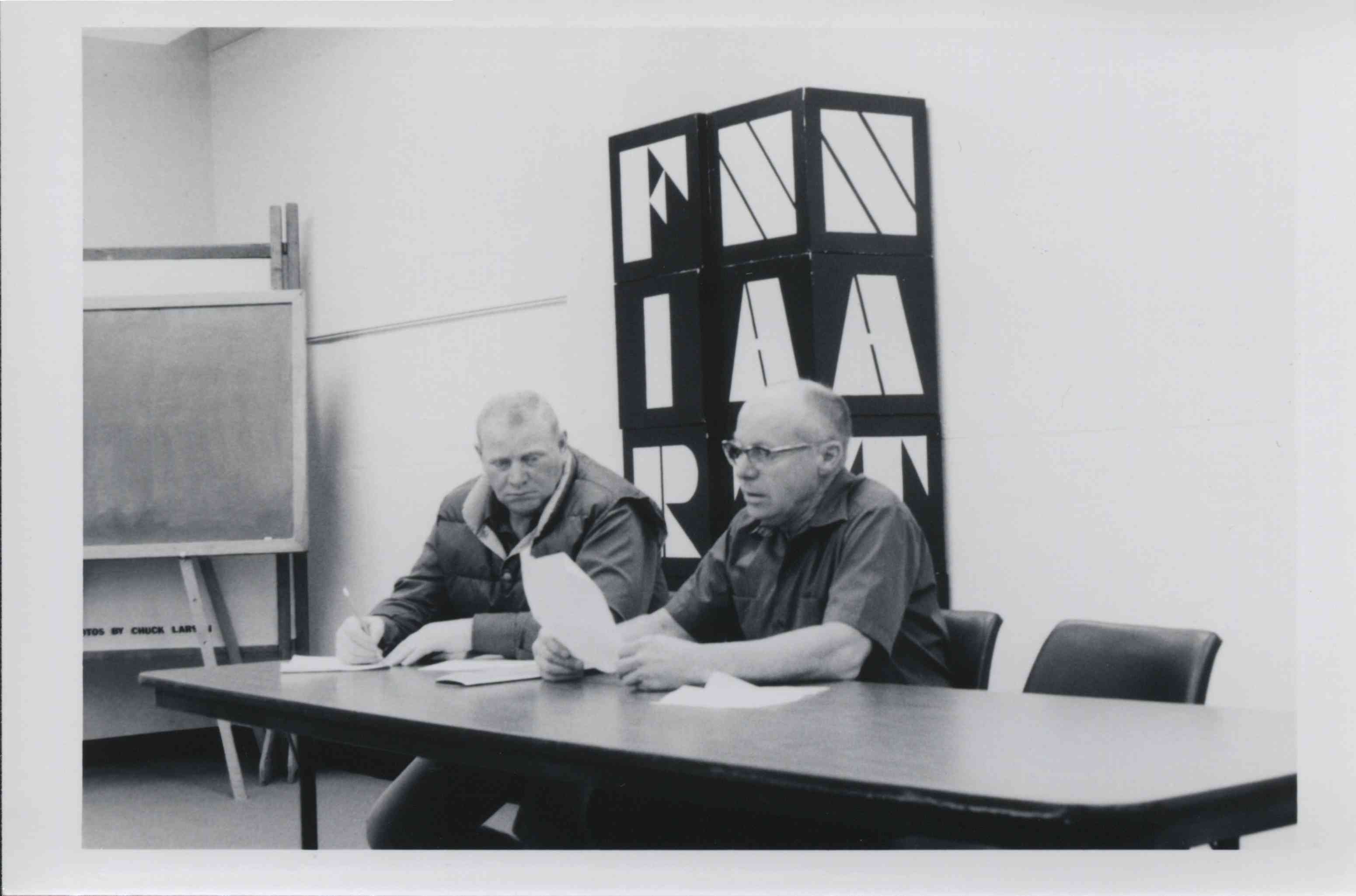 Two Men Reading Document at Table