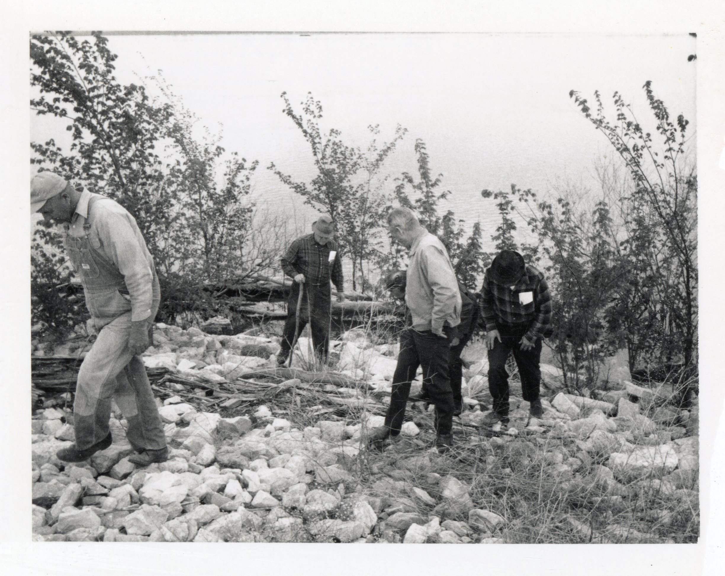 1970? Four men walk along brush and rocks near Mississippi River
