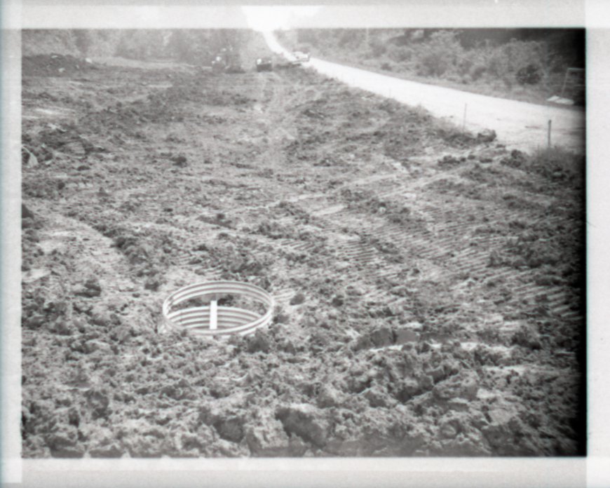 Drainage Pipe Surrounded by Enclosure in Field Next to Road