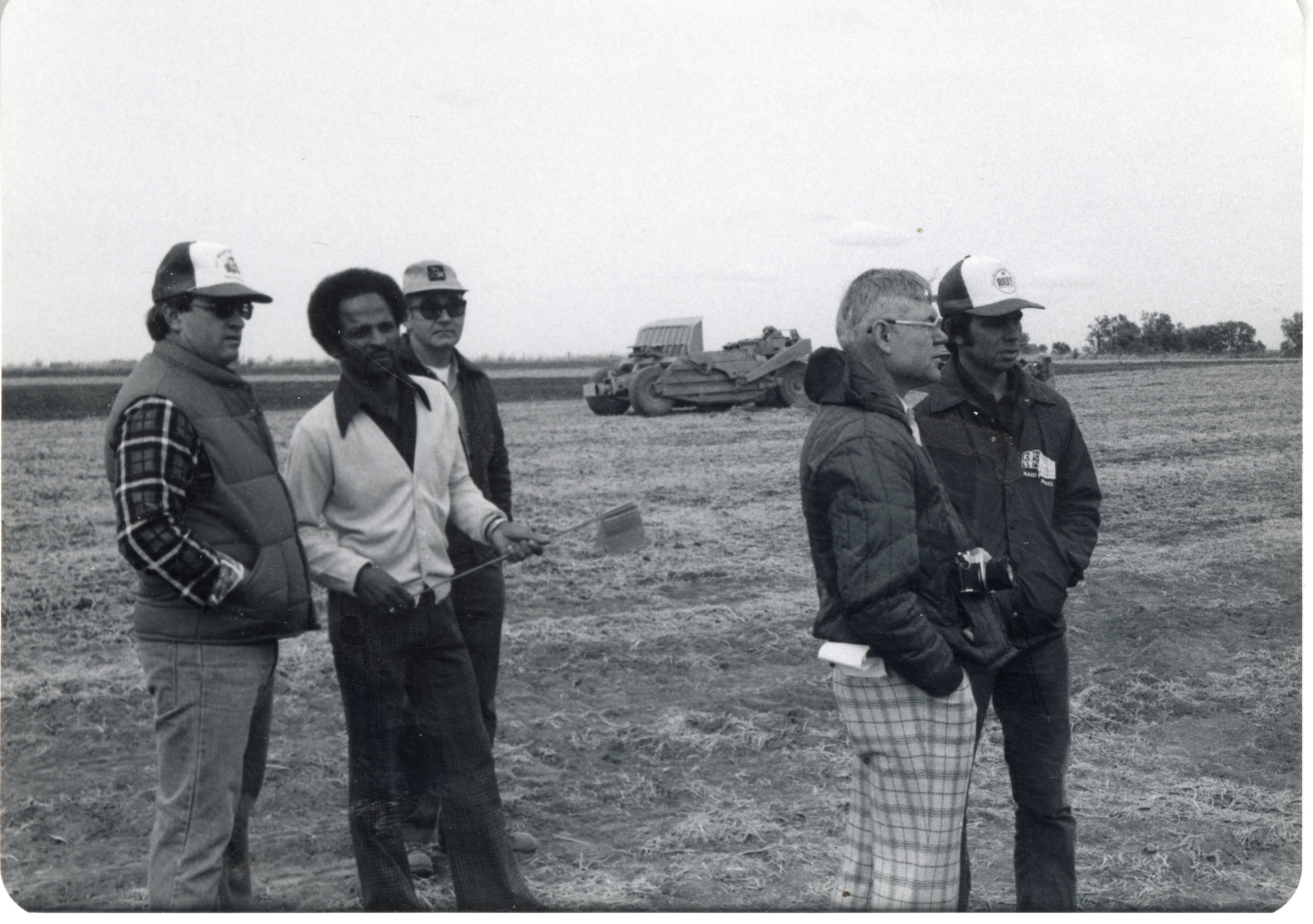 Five men stand near earthmover