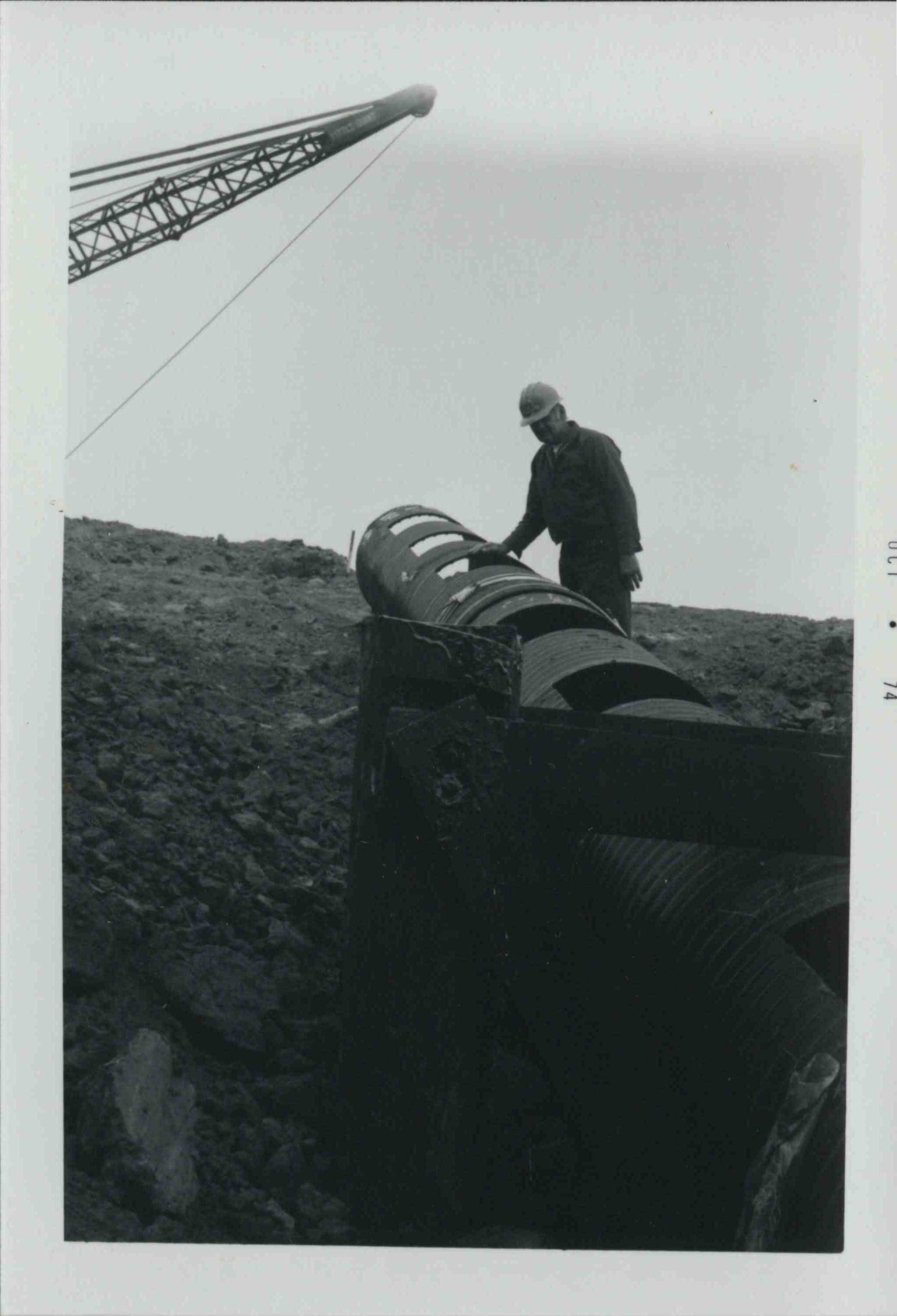 Man wearing hard hat examines pipe on hill