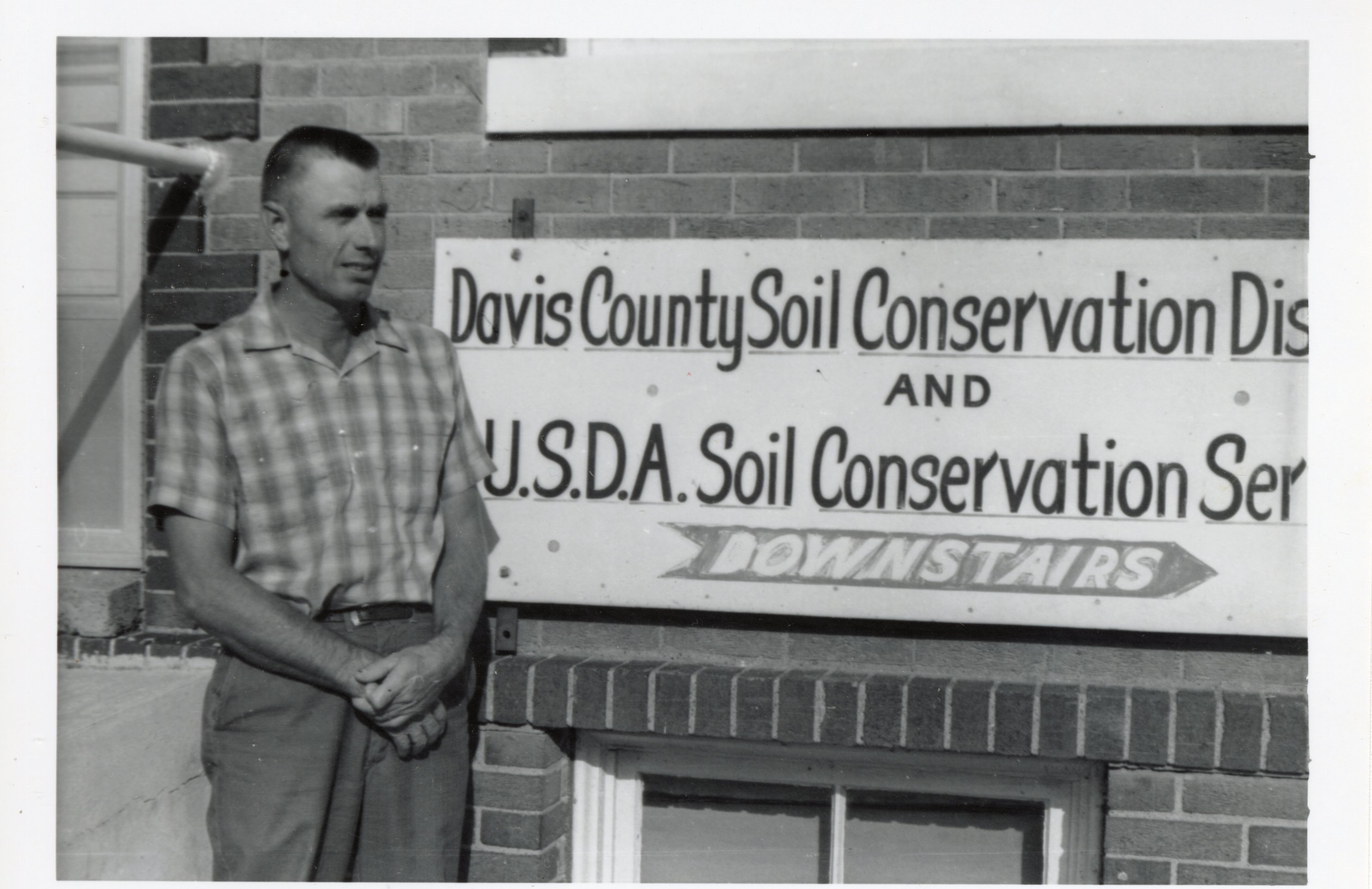 1964 - Sam Botts, Jr. stands beside Davis County Soil Conservation District sign