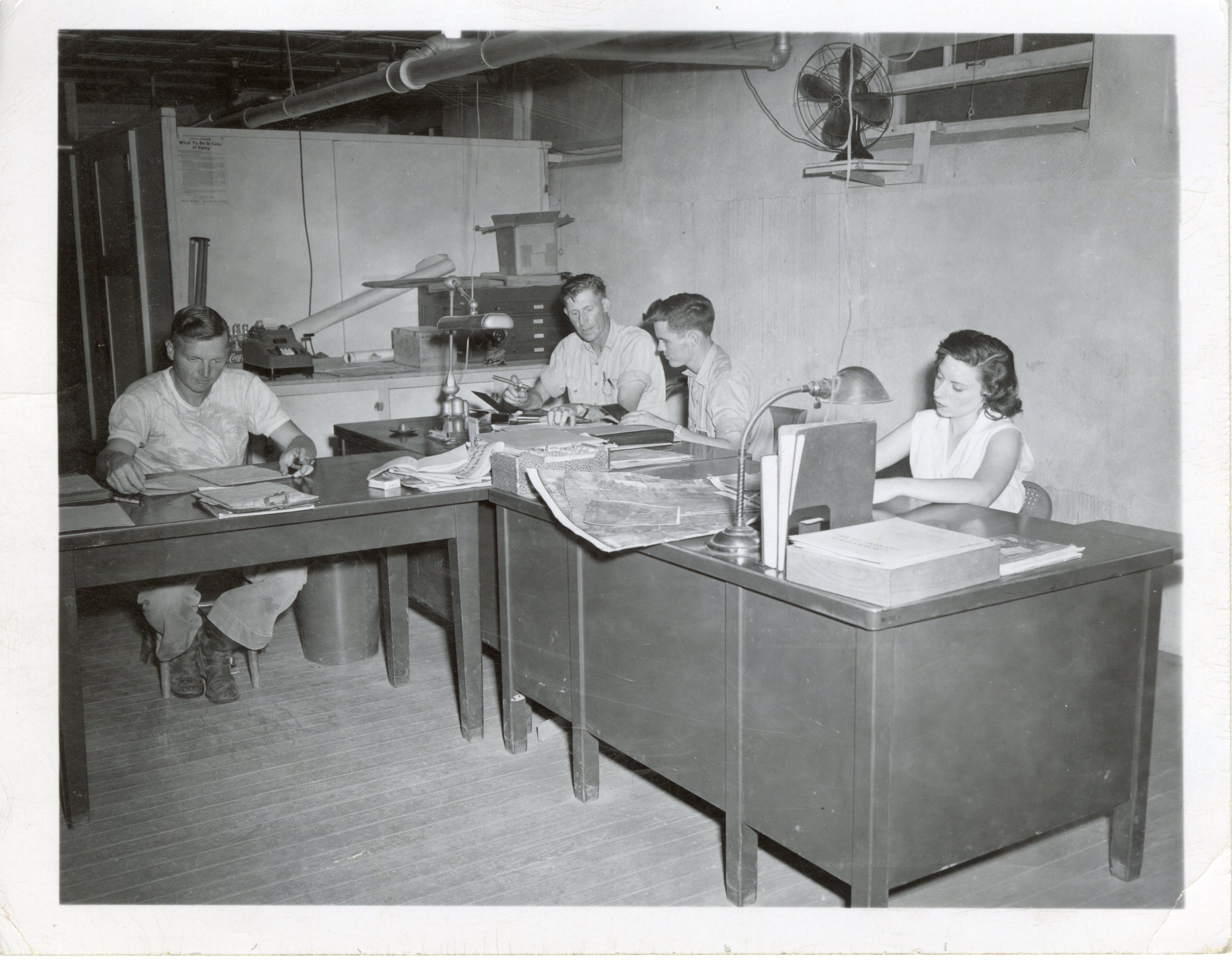 Three men and one woman work at office tables