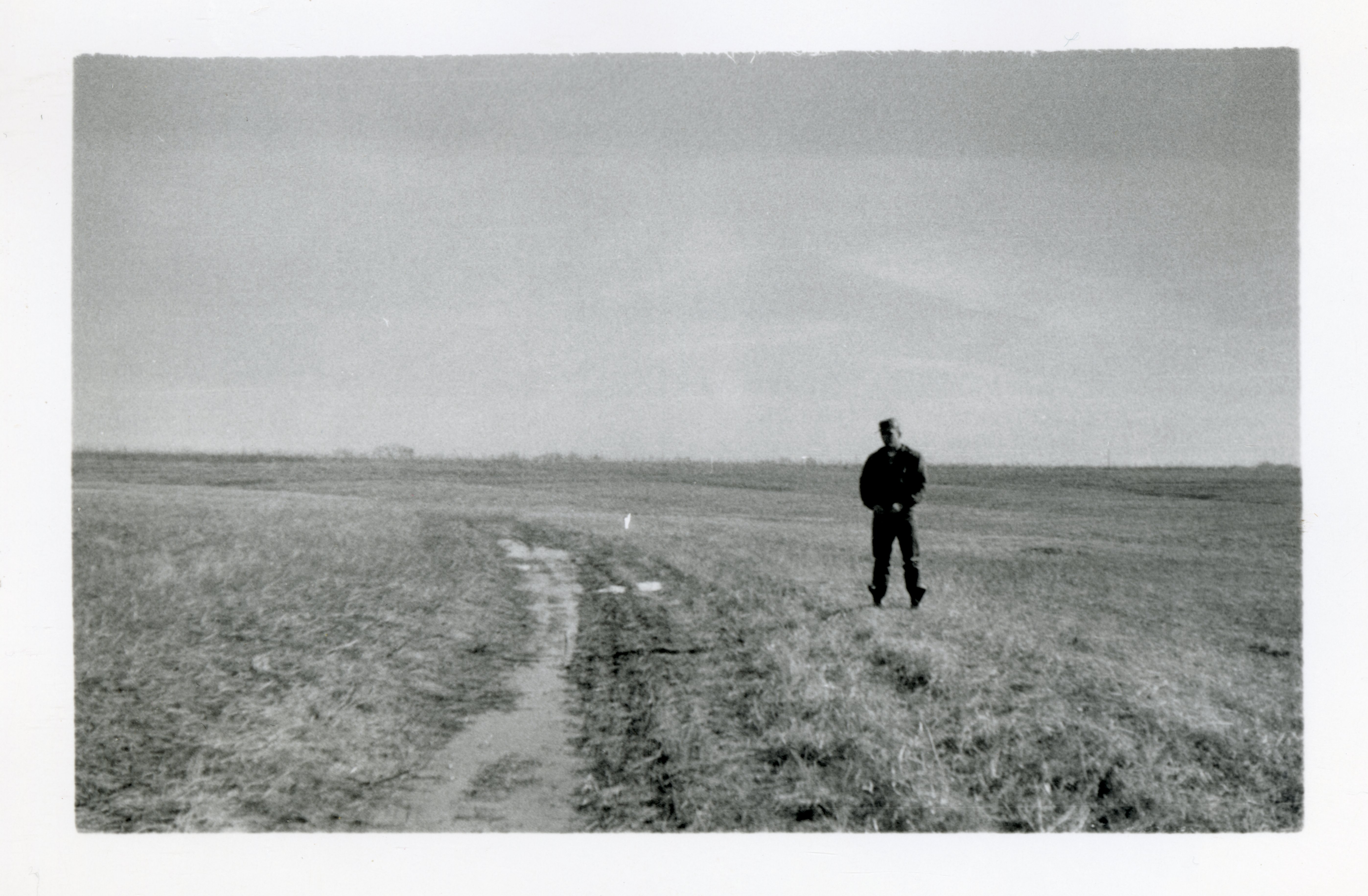Unidentified Man Walks in Pasture Beside Water Running Down Field