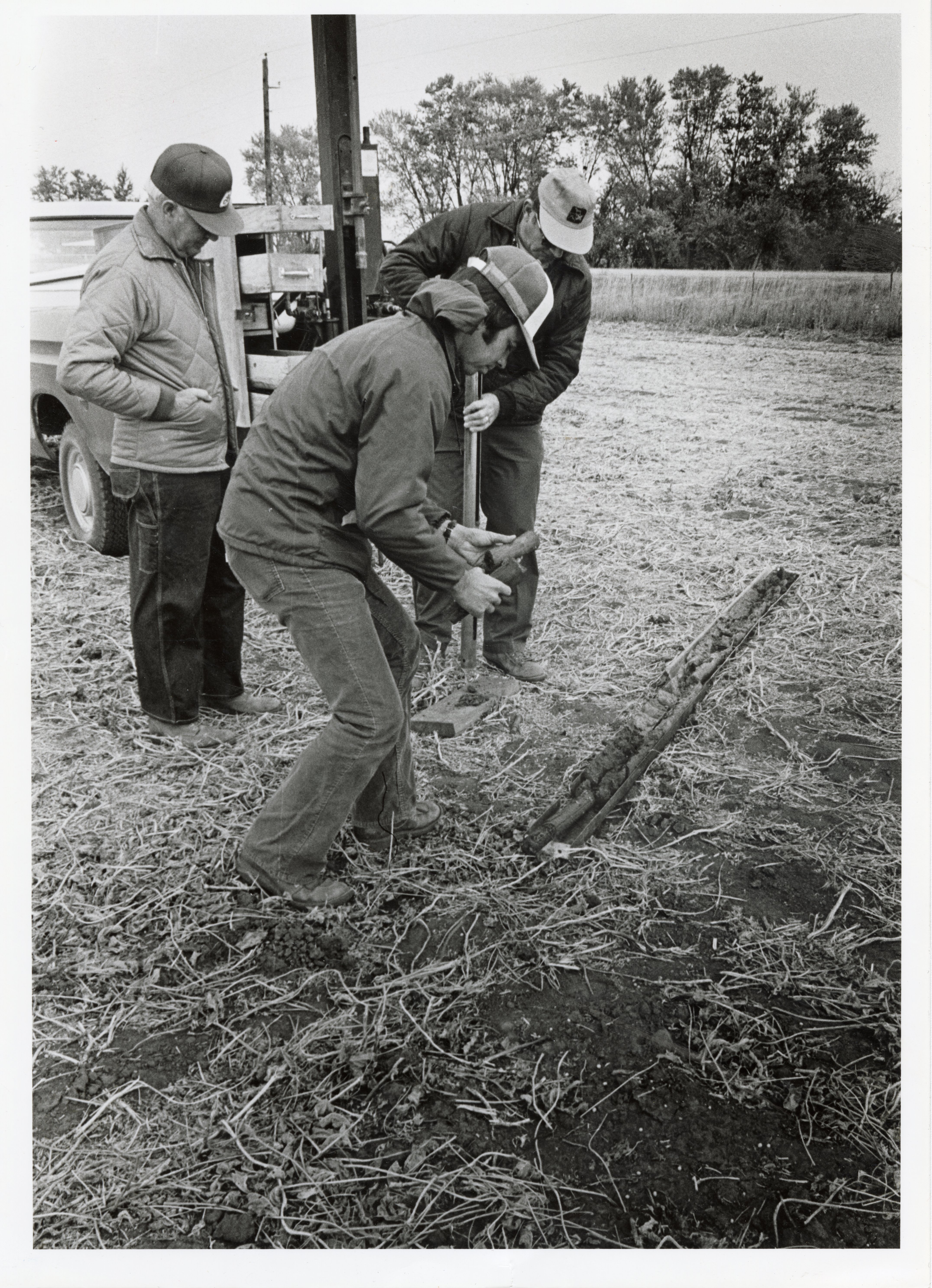 1979  Two men plant stake in a field while third man watches
