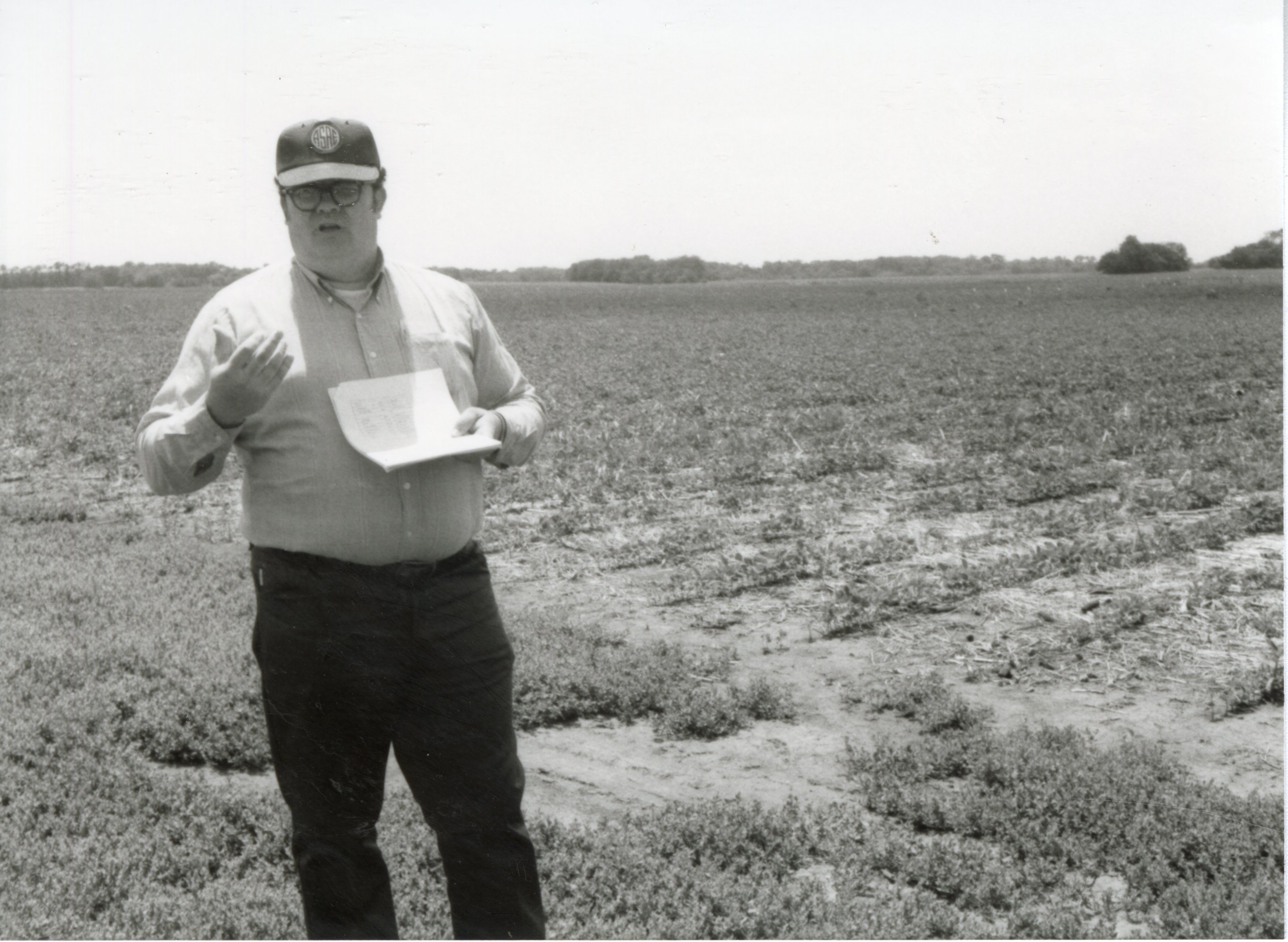 Unidentified man in glasses and hat in field speaks to unseen audience
