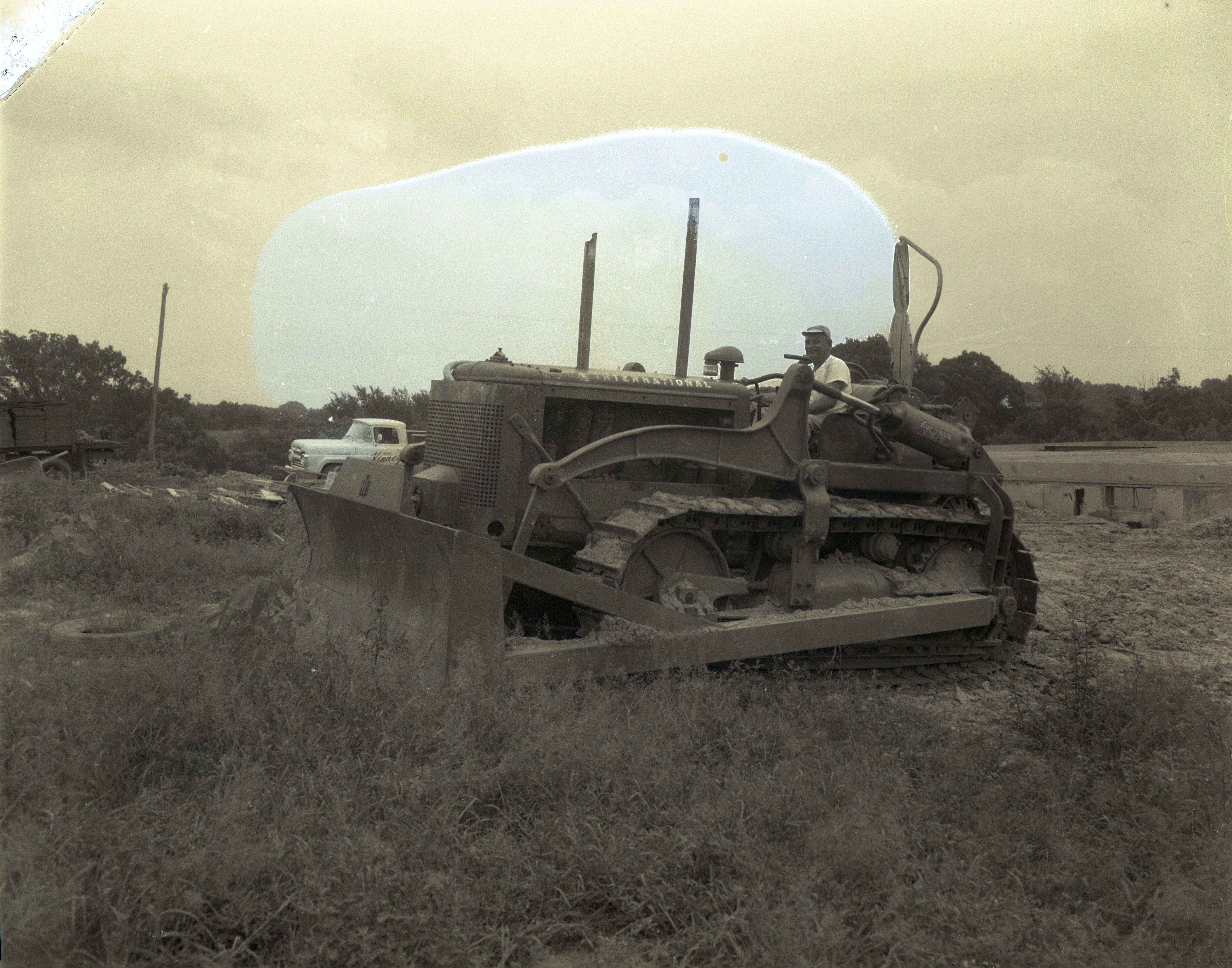 Man drives International bulldozer with Bucyrus Erie bulldozer blade in a grassy field