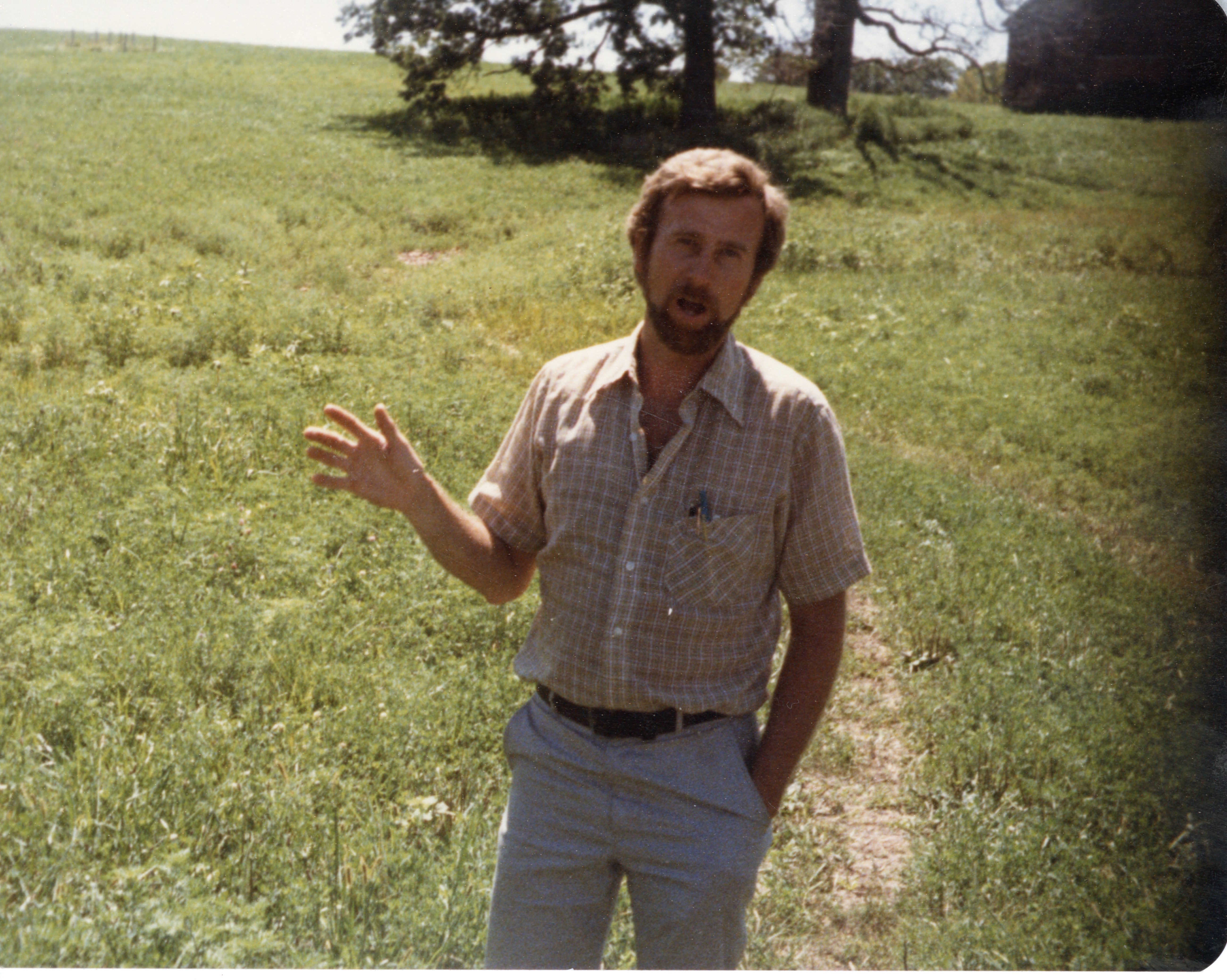 Unidentified Bearded Man Talking in Field with Hand Extended