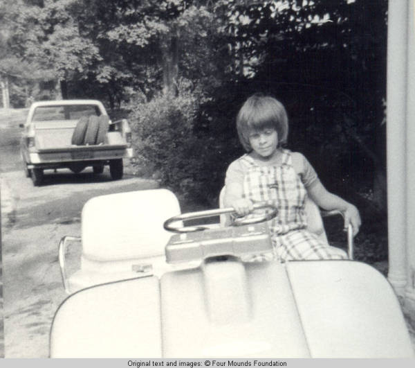 John, Jr. in golf cart with hand on driving bar, looking down
