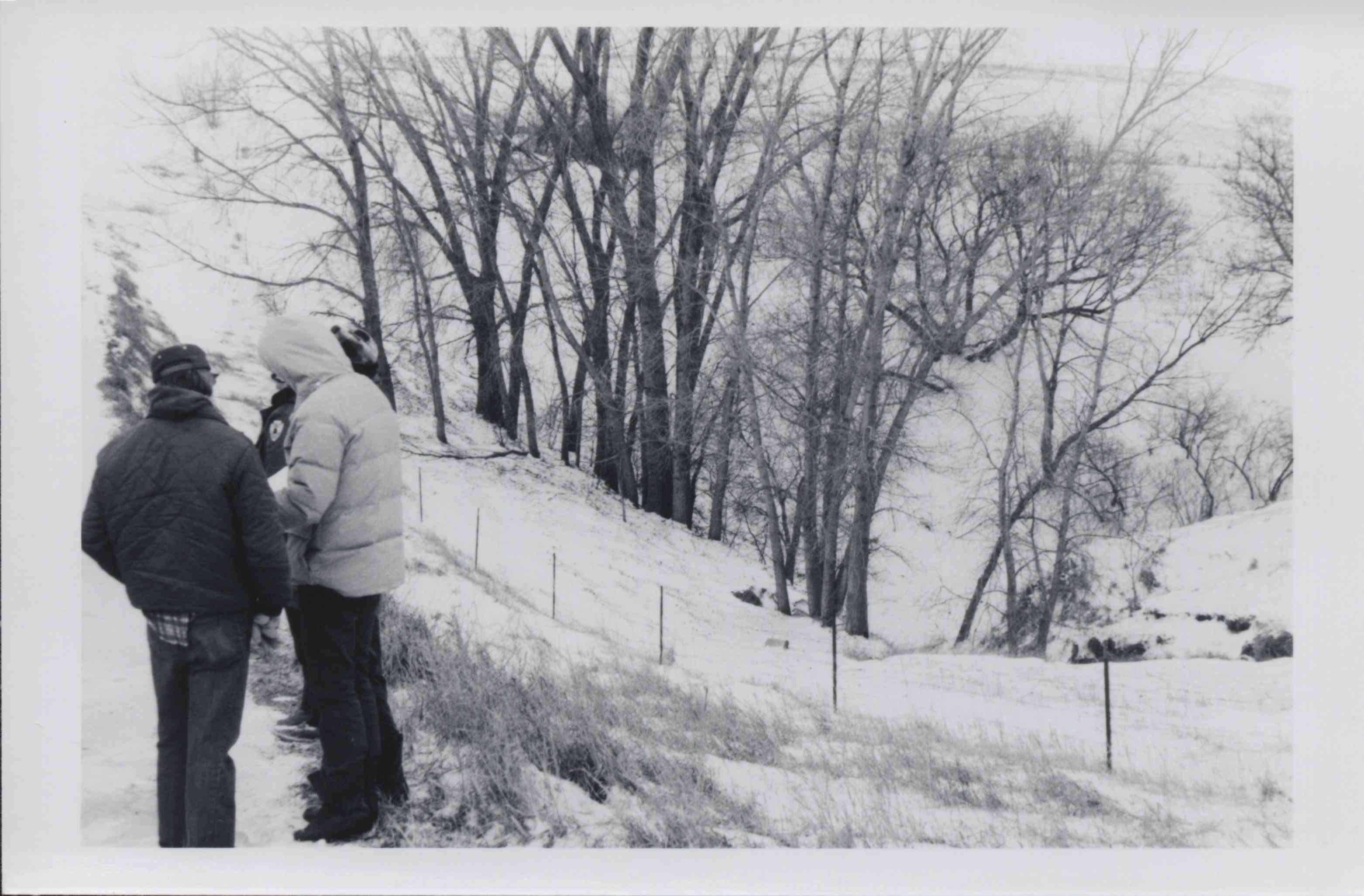 Three men stand in the snow looking at some papers
