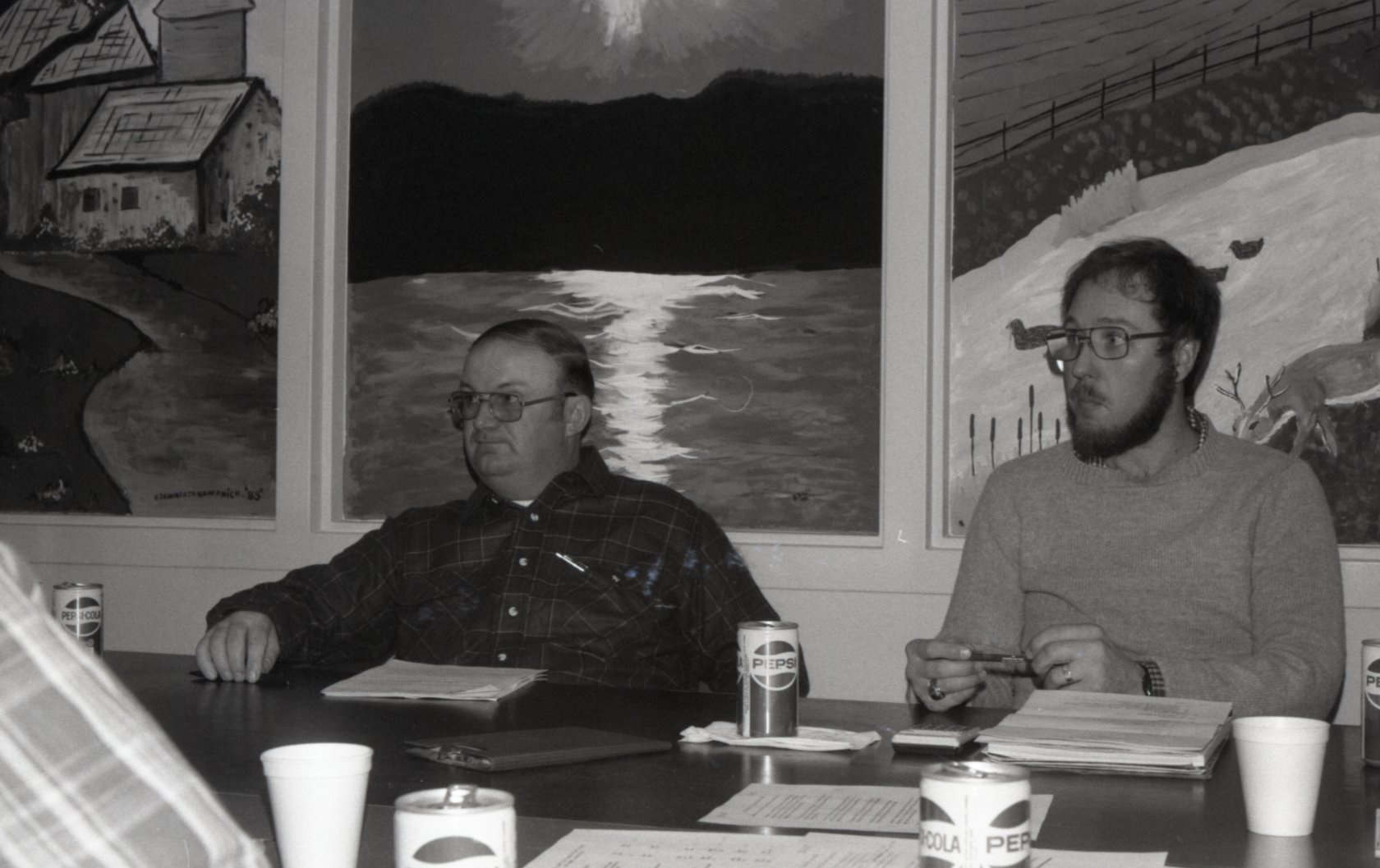 Two unidentified men sit at a table listening at a meeting