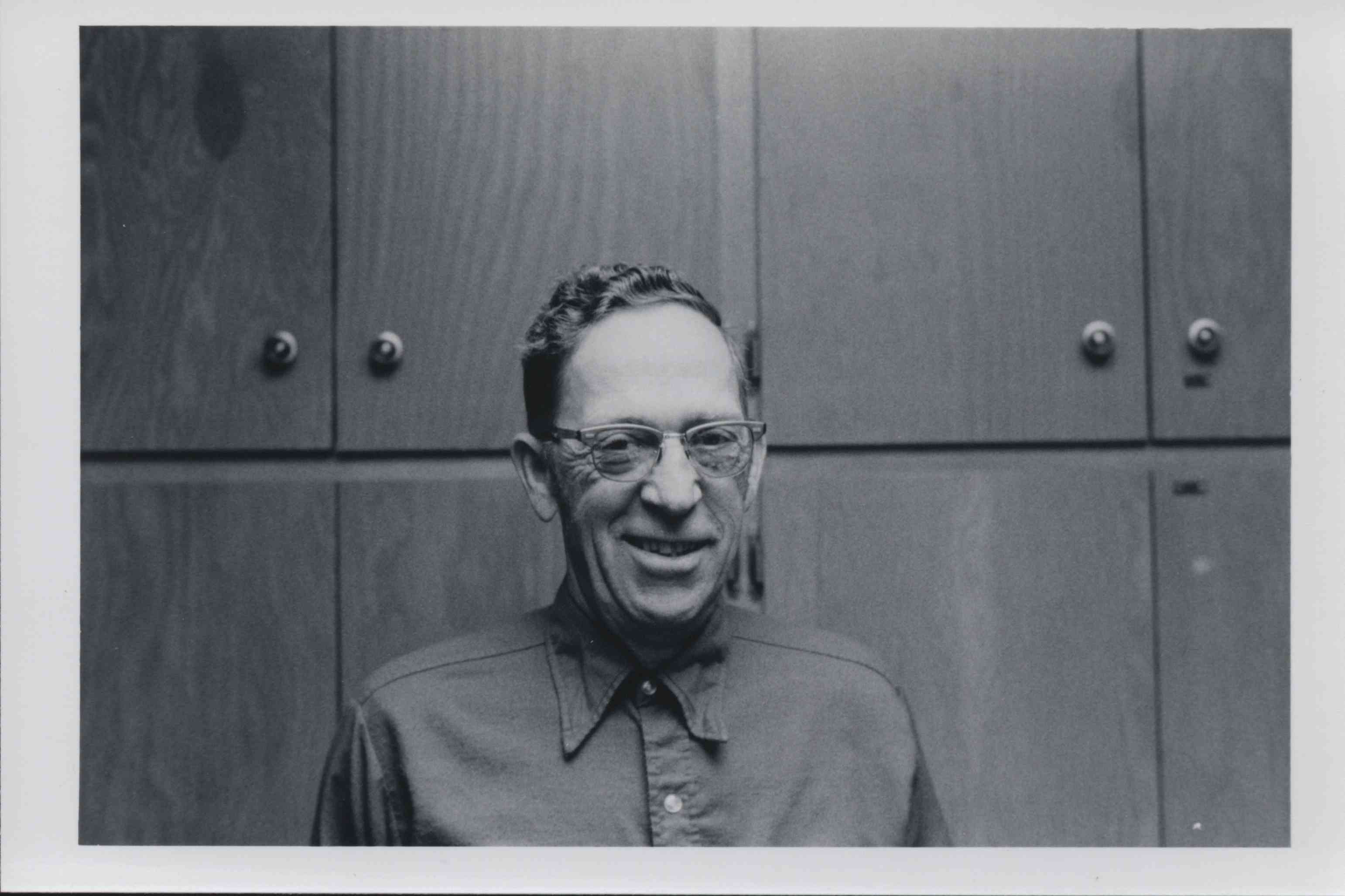 Unidentified Curly-Haired Man with Glasses Stands by Cuphoard
