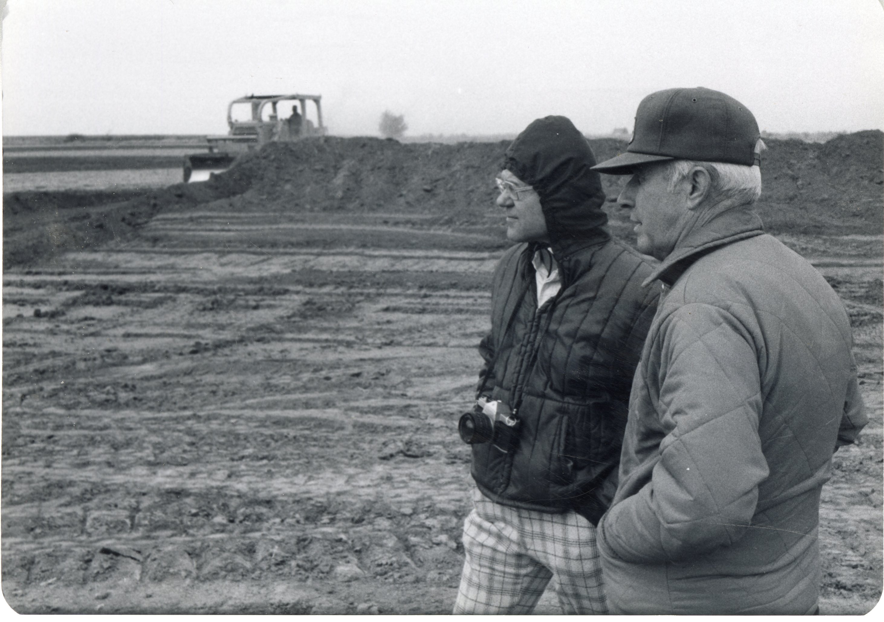Two men stand near earthmover in a field