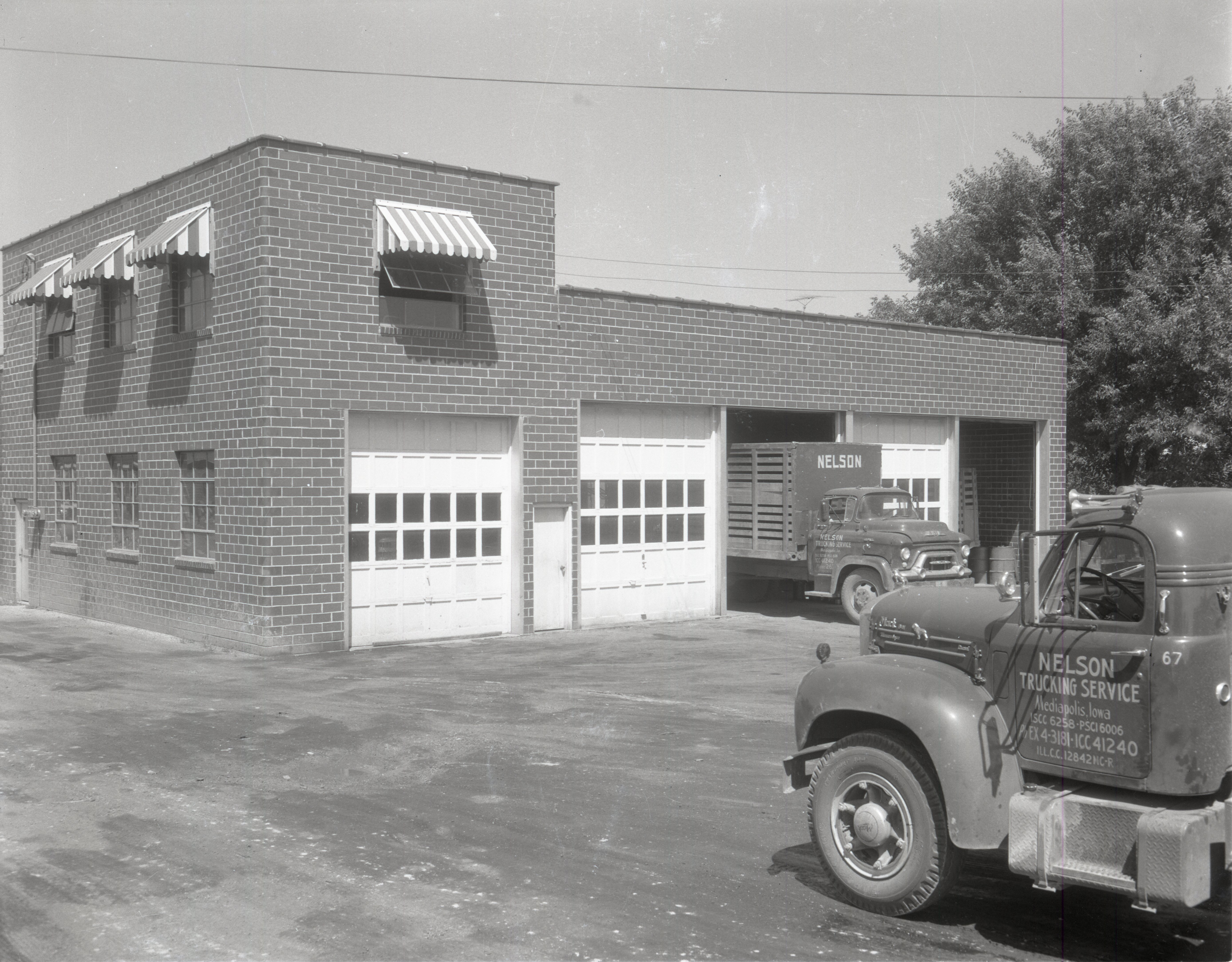 Nelson Trucking Service trucks sit by brick garage