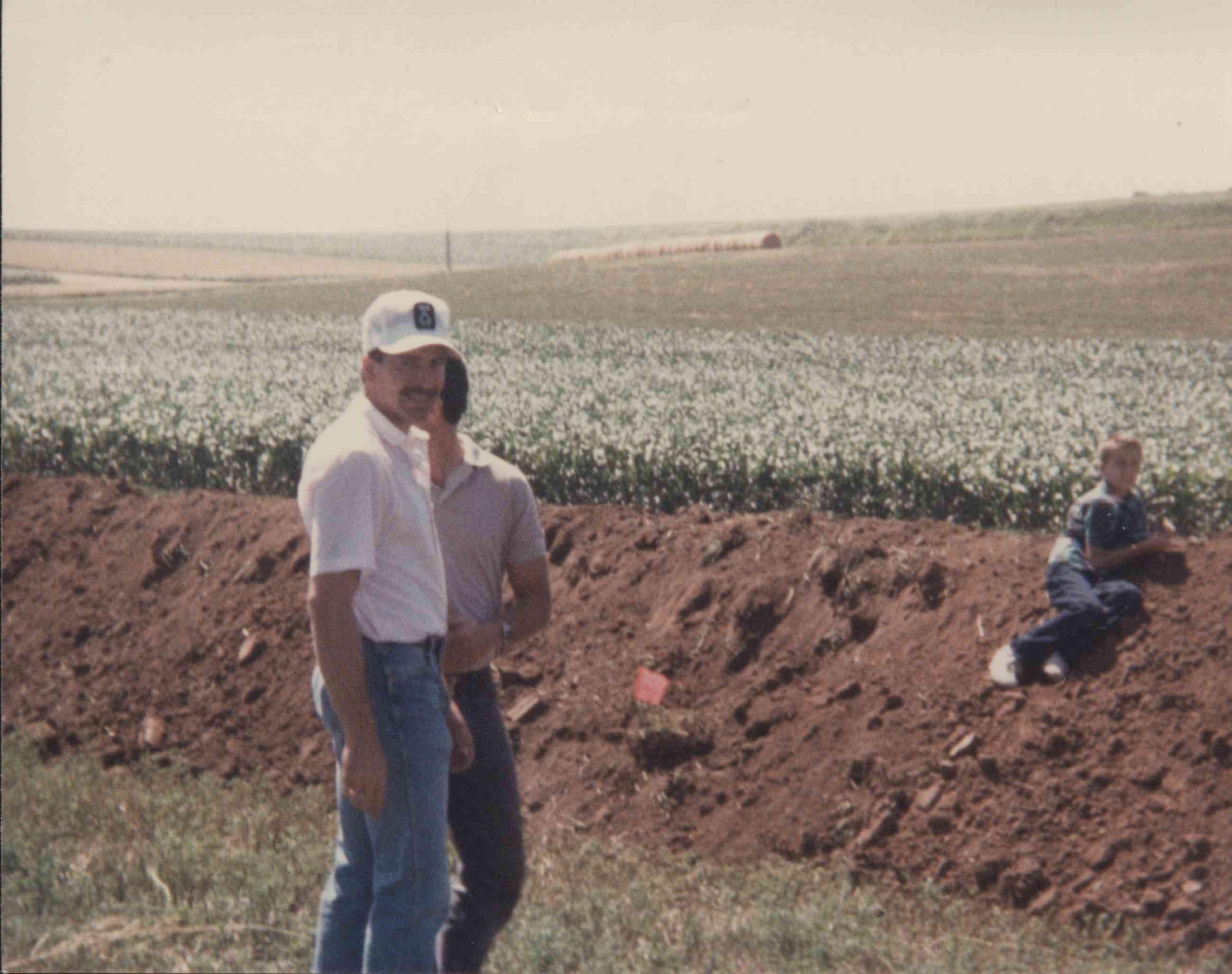 Two men watch boy sitting on bulldozed dirt