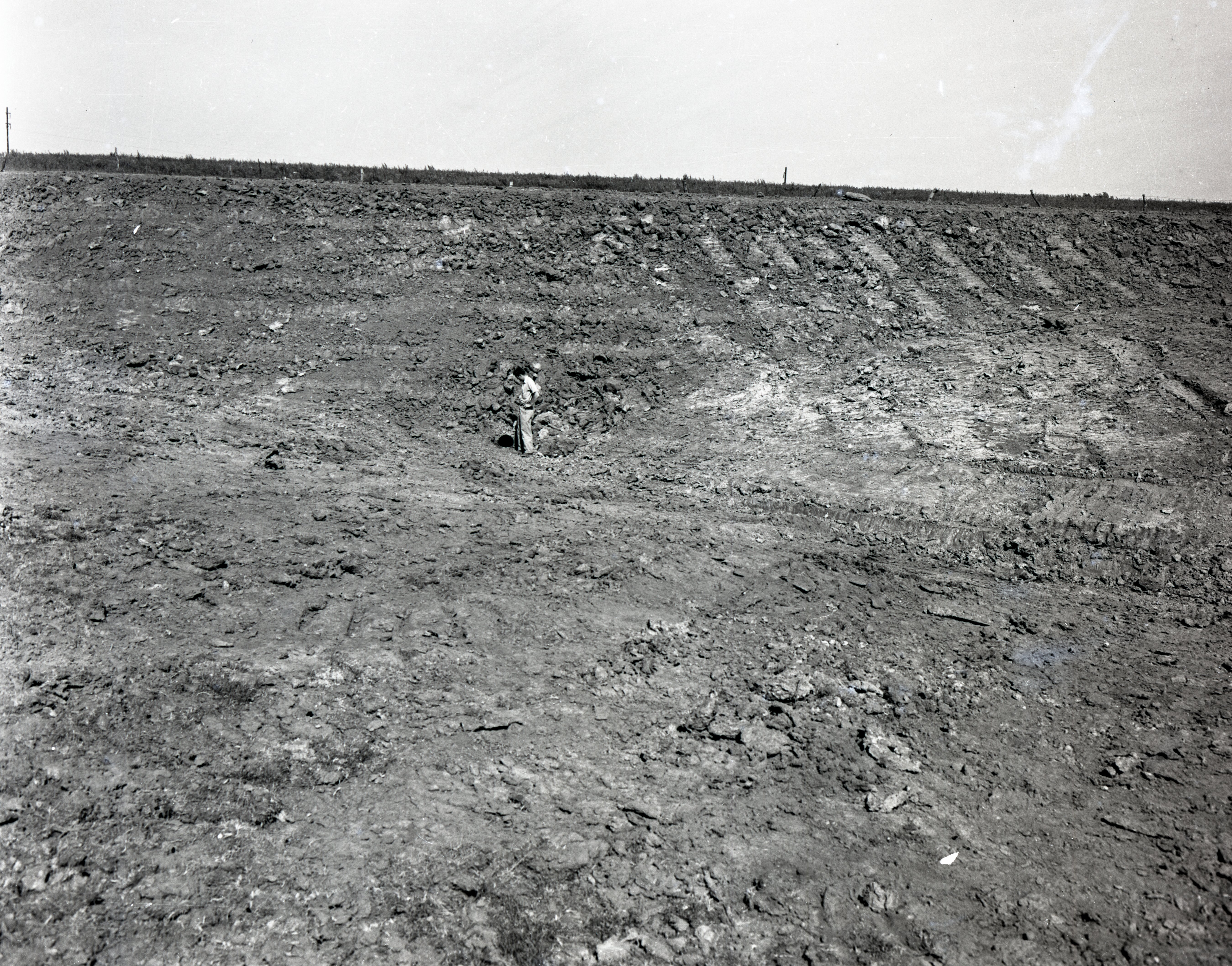 Unidentified Man Looks Down at Pipe in Rocky Soil