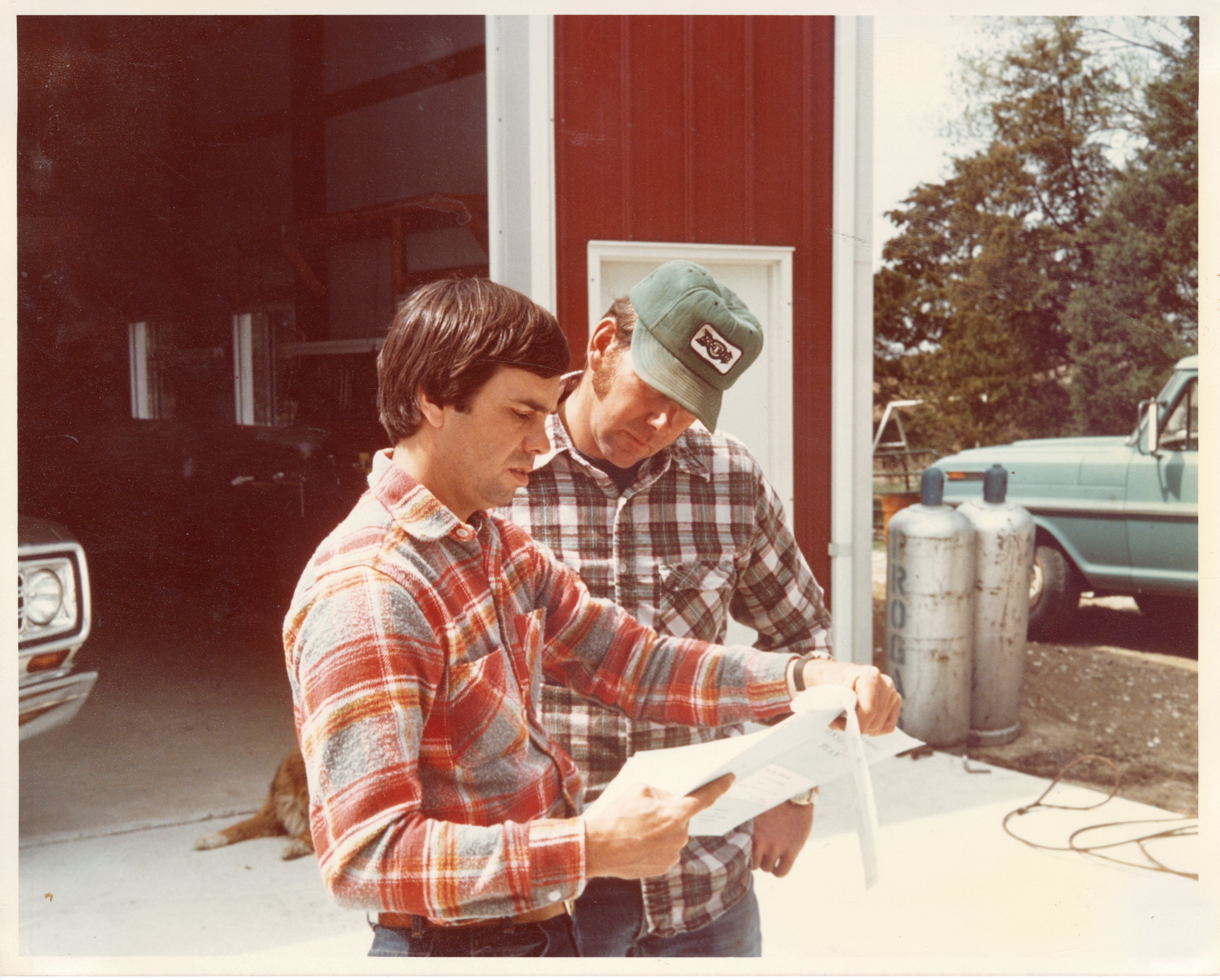 1970s Howard Bright and another man confer over a document that Howard is holding
