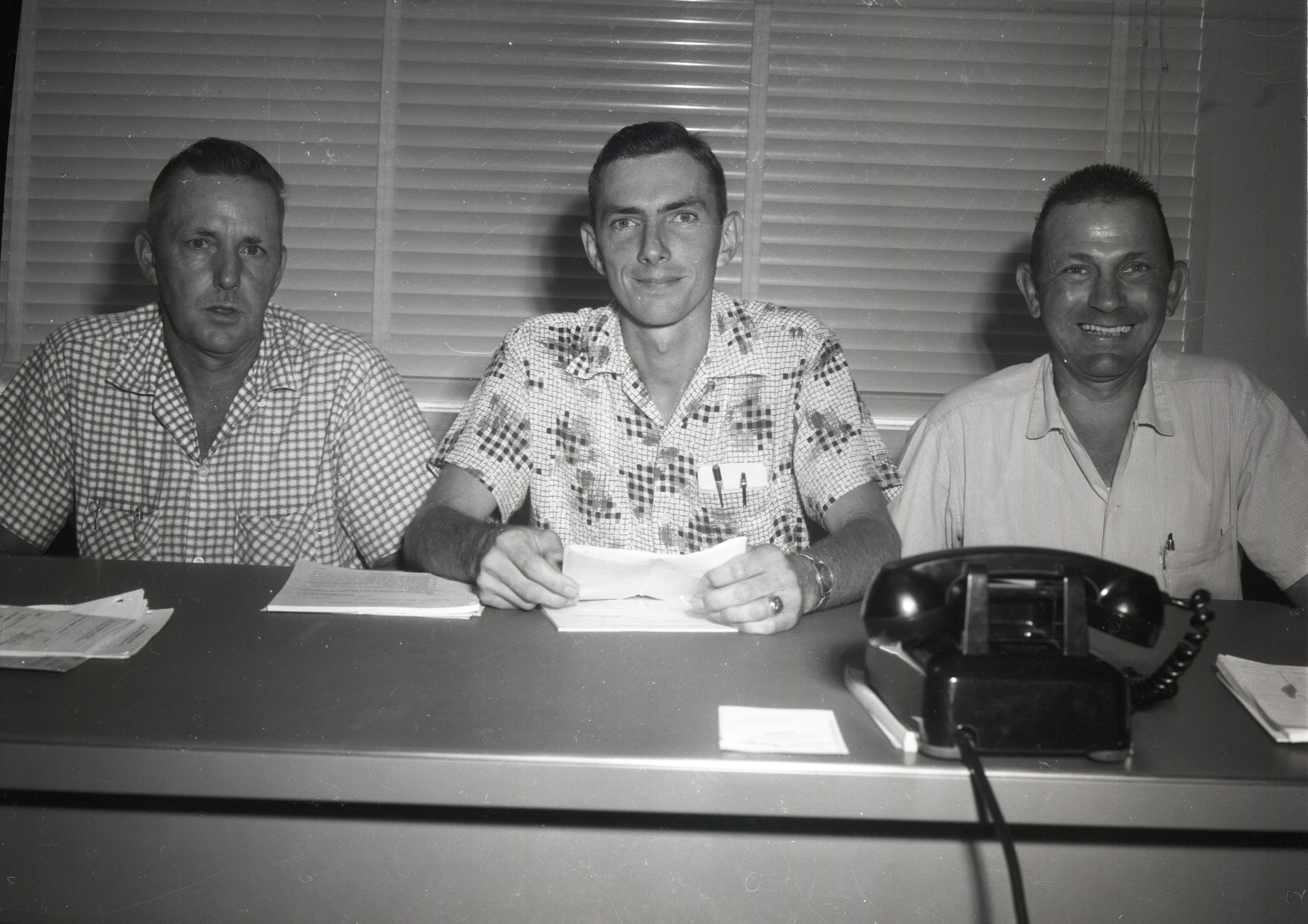 Three unidentified men sit in office at a desk