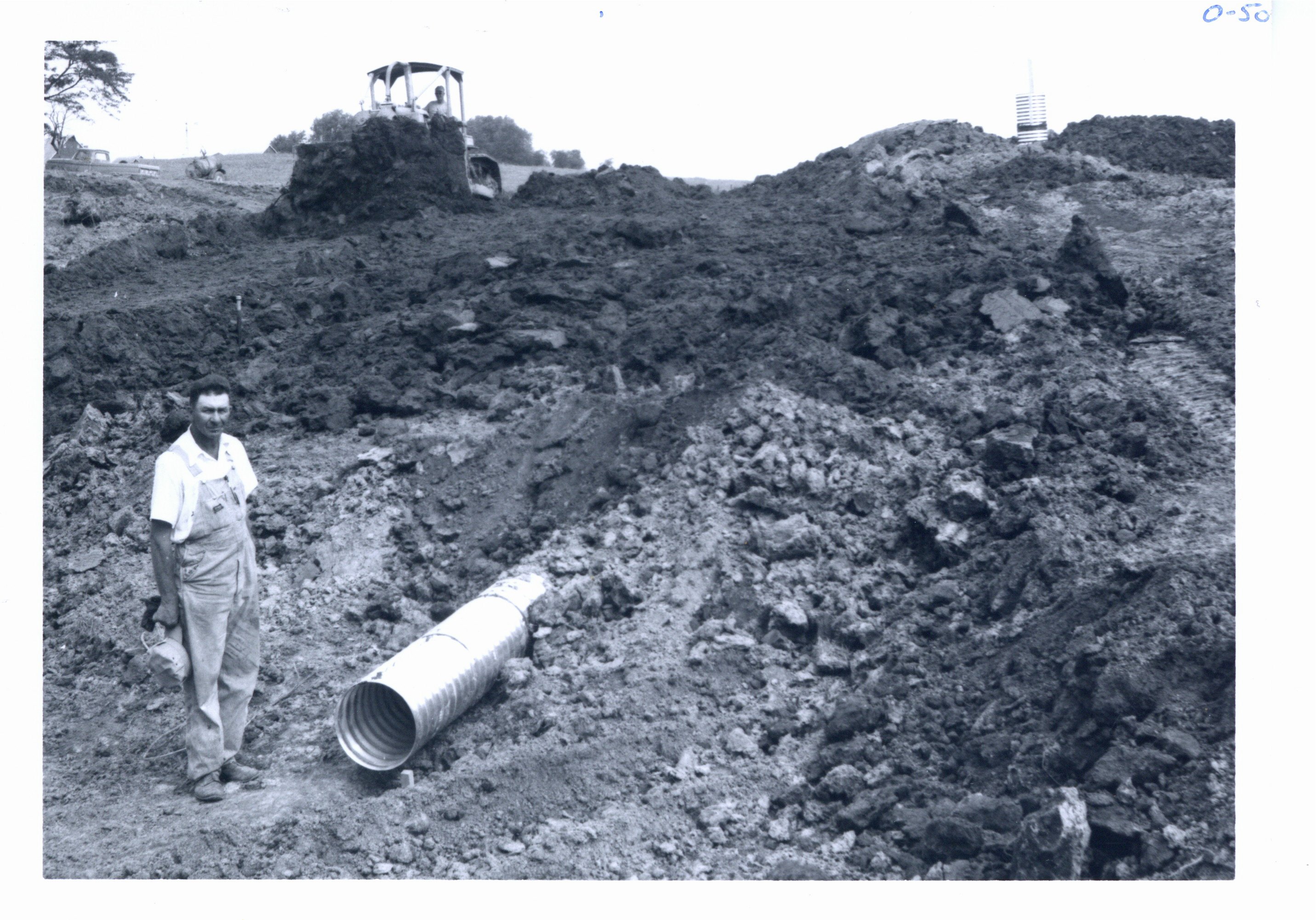 Clyde Small poses beside outlet end of pipe spillway, 1966