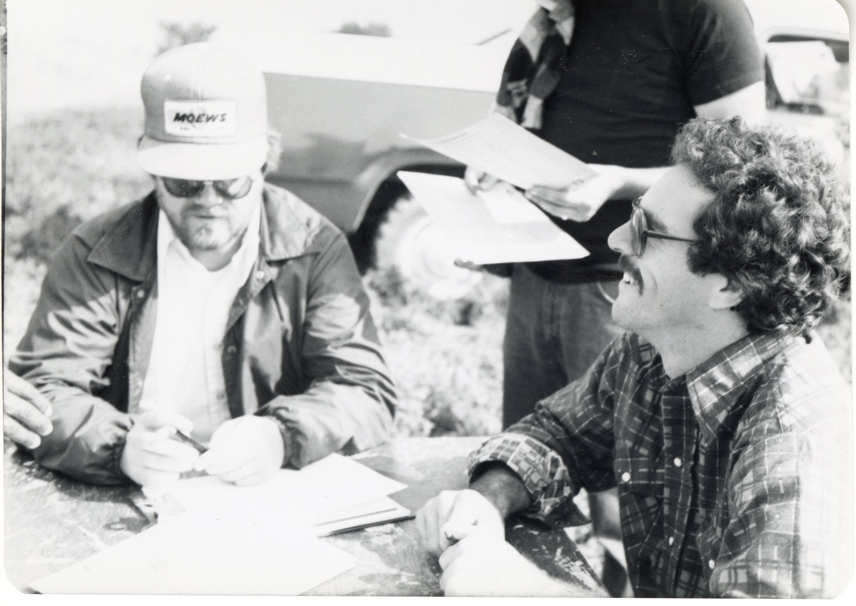 1978 Two men sit at a table in a field