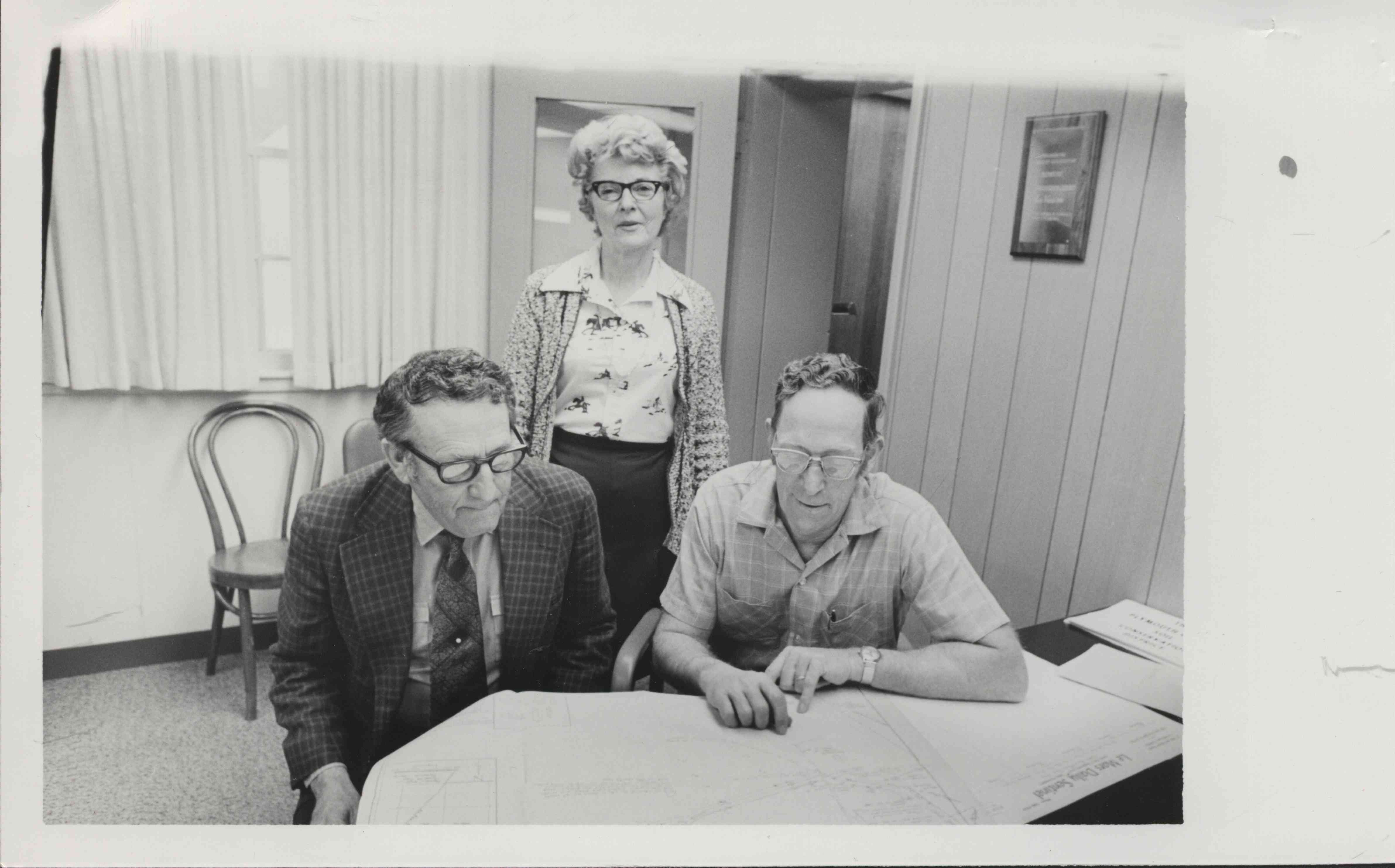Standing Woman and Two Seated Men Looking at Map
