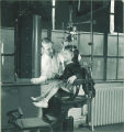 Dentist adjusts a device on a young girl's head while she sits still in a dental chair, The University of Iowa, 1940s
