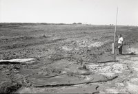 Man Stands by TOT Pipe in Field