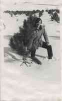 Man with mustache examines small pine tree in the snow