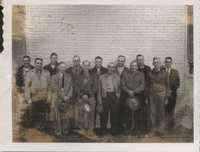 Gathering of unidentified men posing in front of white brick wall