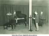 Carl Menzer standing near grand piano in radio broadcast, The University of Iowa, 1924