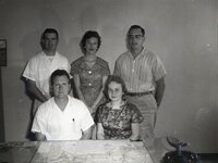 Three men and two women pose for picture in front of map