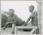 Two young farm workers leaning on a fence