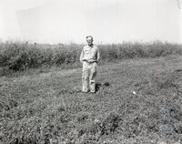 Unidentified man wearing glasses with hands behind his back stands in field