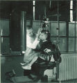 Dentist adjusts a device on a young girl's head while she sits still in a dental chair, The University of Iowa, 1940s
